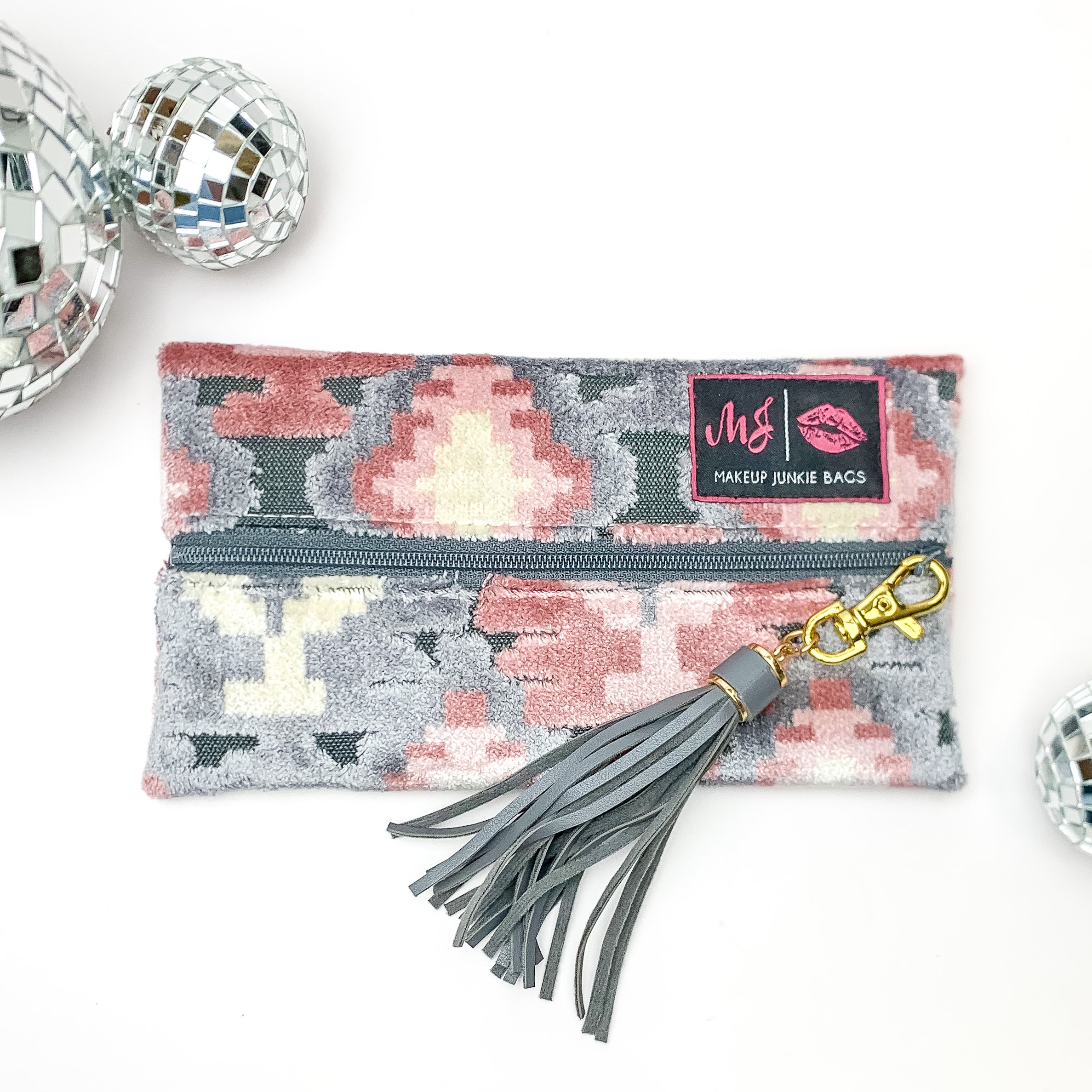 Pictured on a white background with disco balls at top is a mini lay flat bag in a blush aztec print. This bag includes a middle zipper and a tassel.