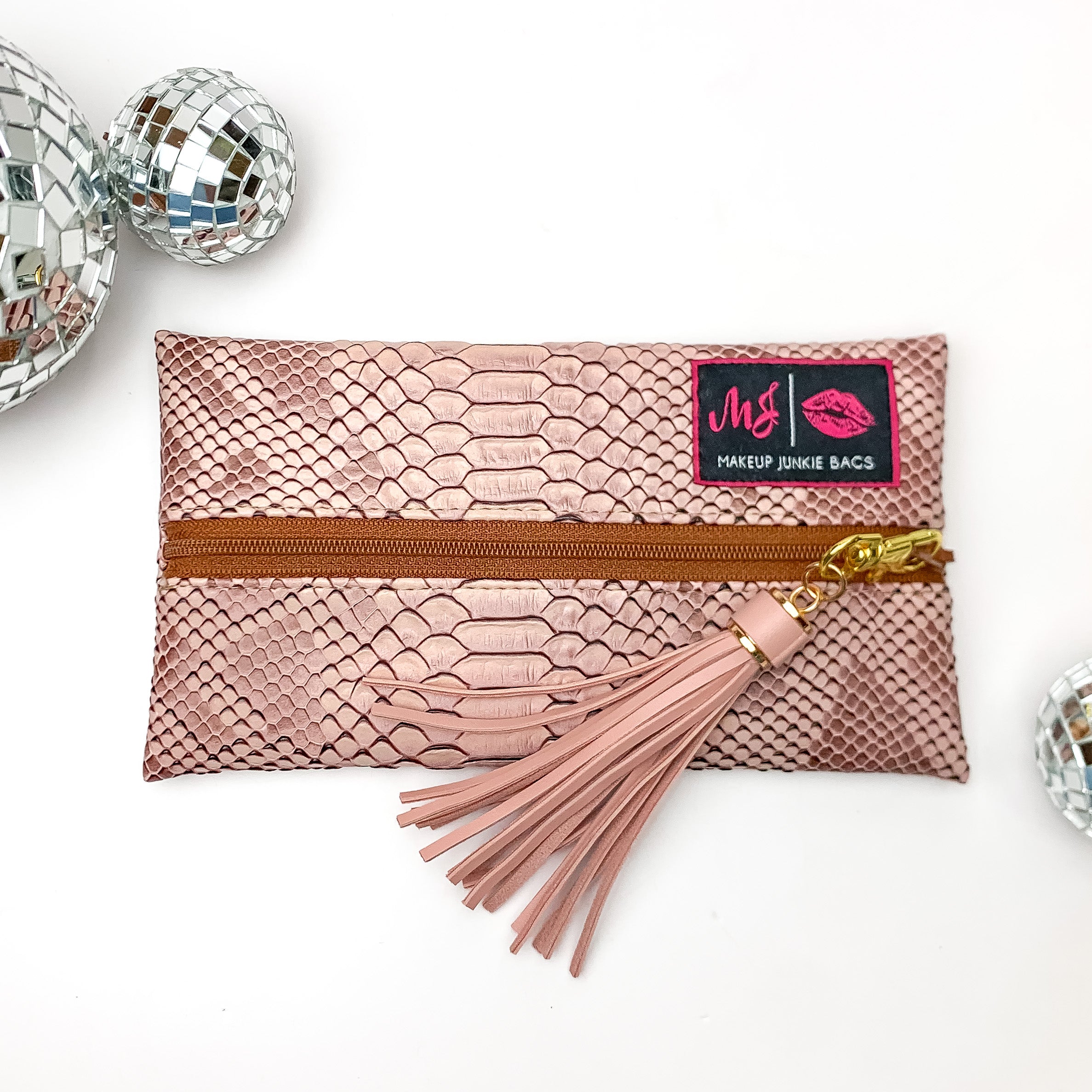 Pictured on a white background with disco balls at top is a mini lay flat bag in a copper snake print. This bag includes a middle zipper and a tassel. 