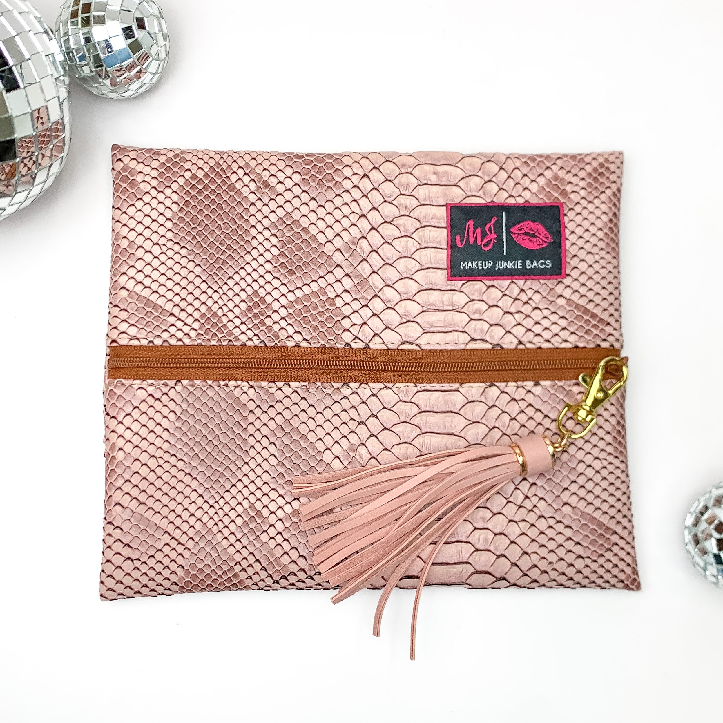 Pictured on a white background with disco balls at top is a mini lay flat bag in a copper snake print. This bag includes a middle zipper and a tassel.