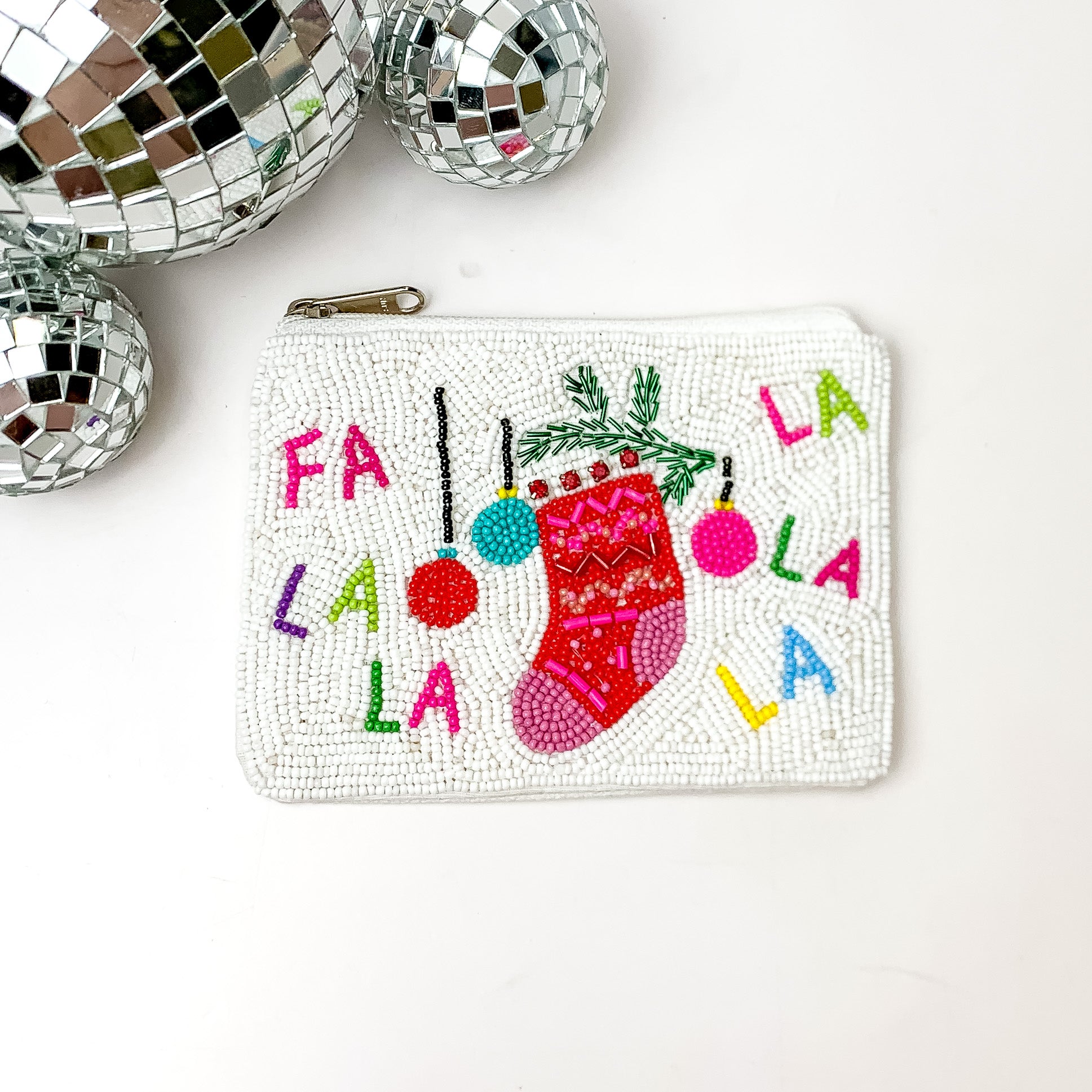 White beaded coin purse with the words FA LA LA in multicolors. This coin purse also has mistletoe, a stocking, and ornaments. This coin purse is pictured on a white background with disco balls in the top left corner. 
