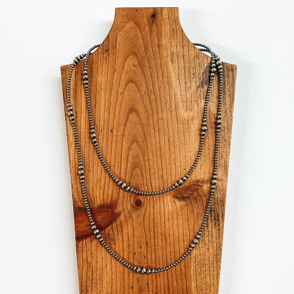 This is a silver beaded necklace pictured on a piece of wood with a white background.