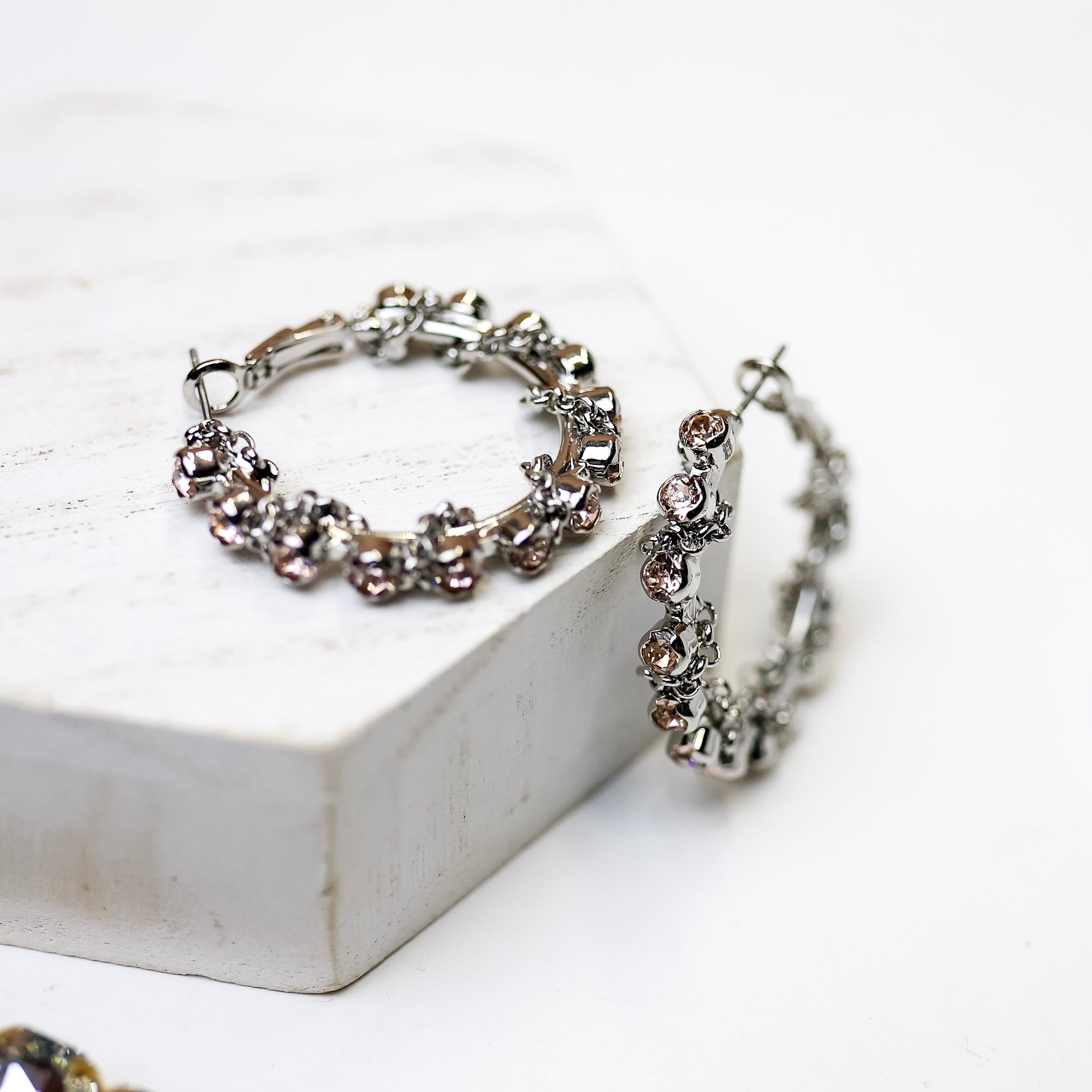 A pair of silver-tone hoop earrings with blush pink crystals and a chain detail. Pictured on a white background.