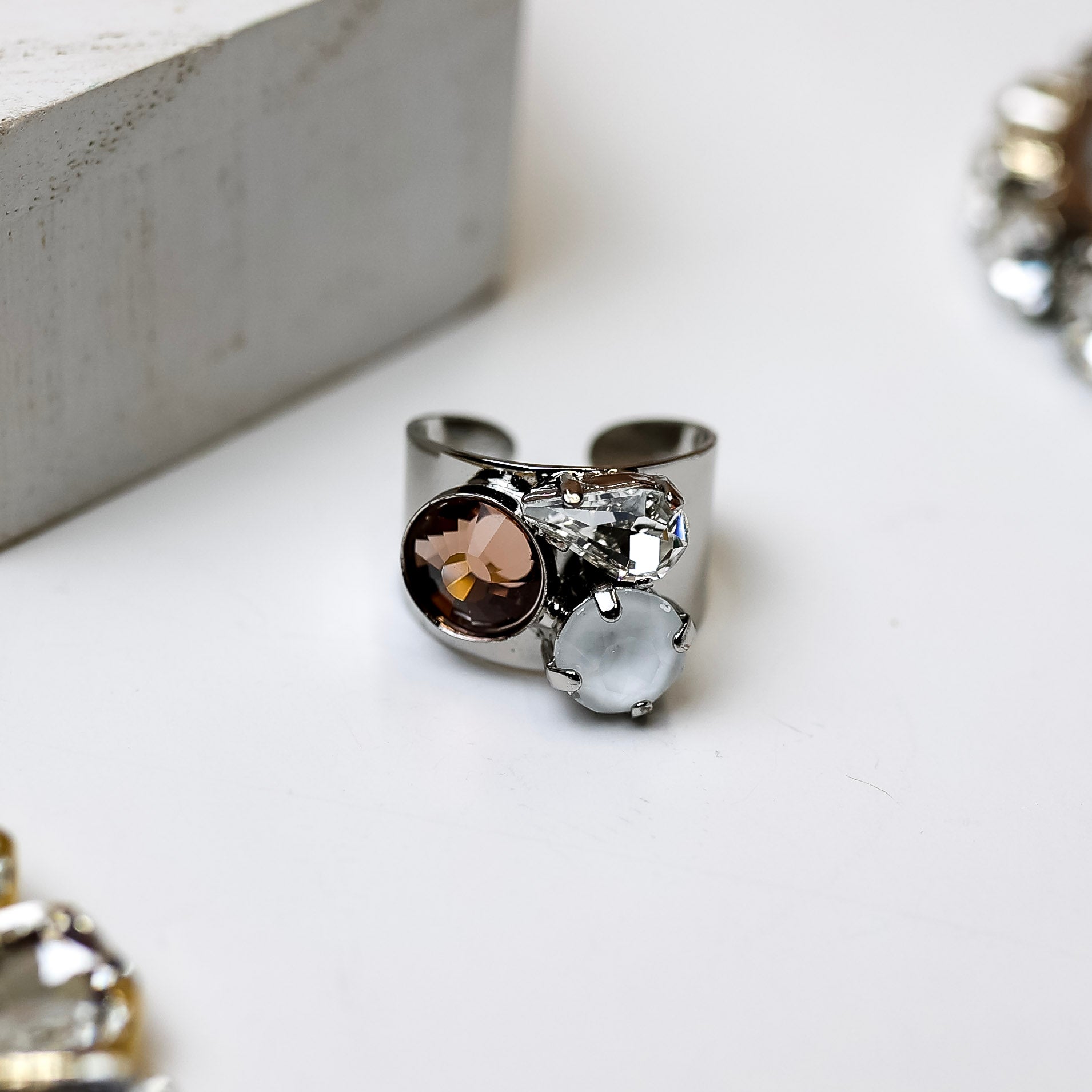 A silver tone adjustable ring with ivory, clear, and topaz crystals pictured on a white background.