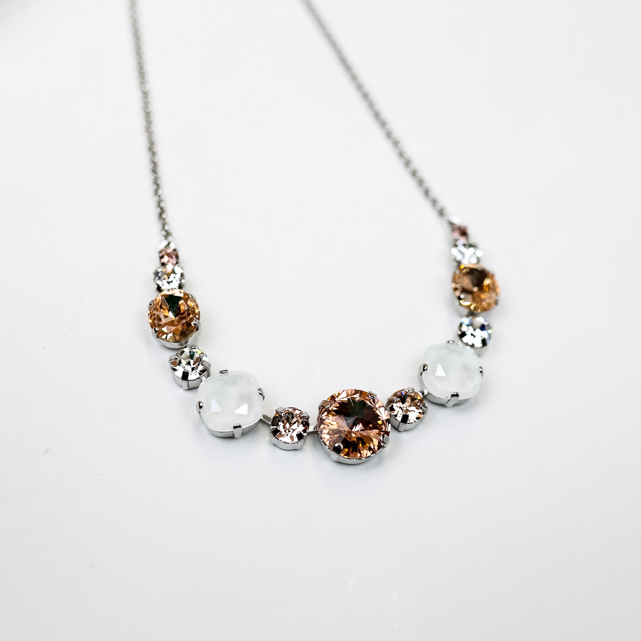 A silver-tone chain necklace with a mix of cushion cut crystals in different sizes and alternates in ivory, clear, and blush color crystals.