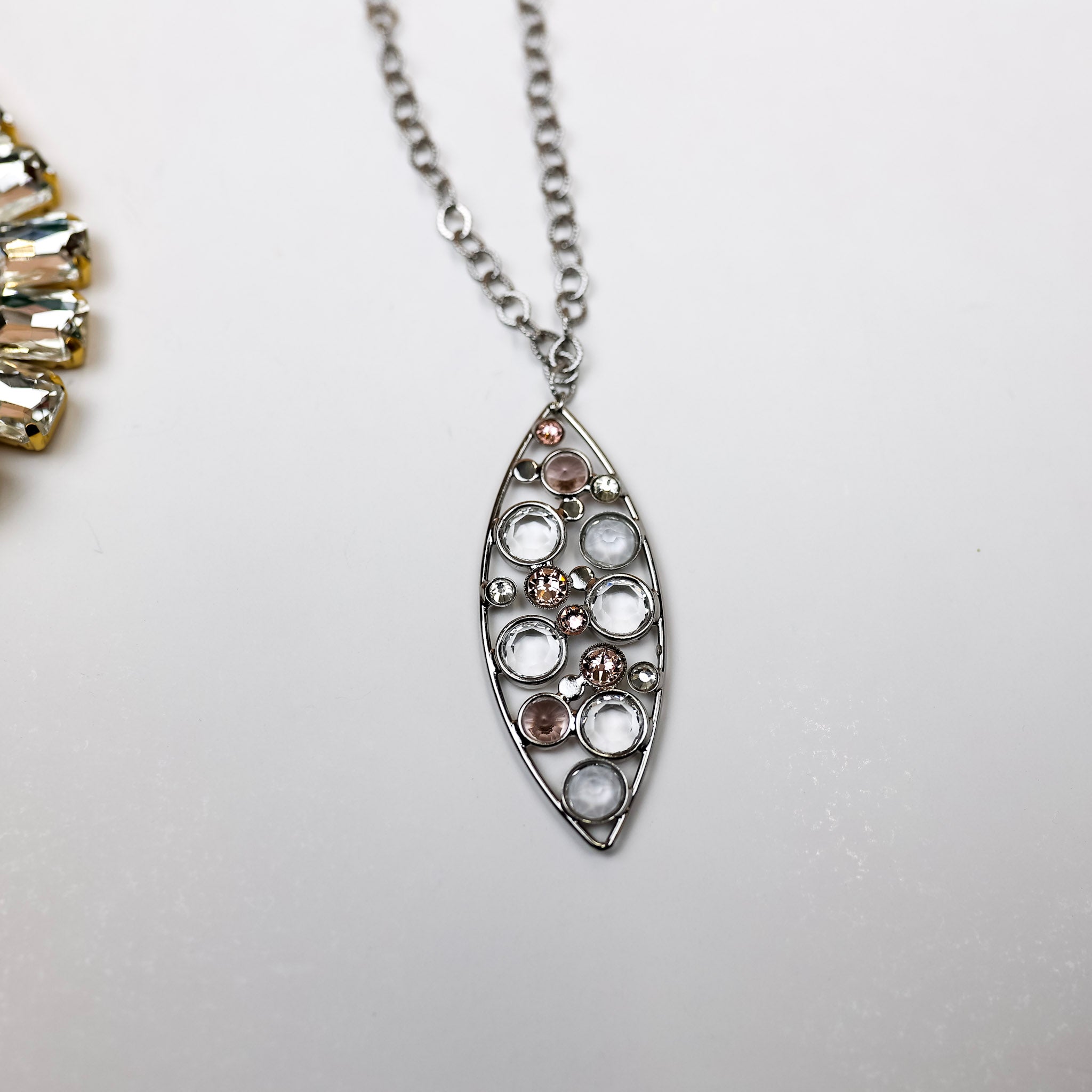 A long silver-tone necklace with an oval outline pendant and crystals. Pictured on a white background.