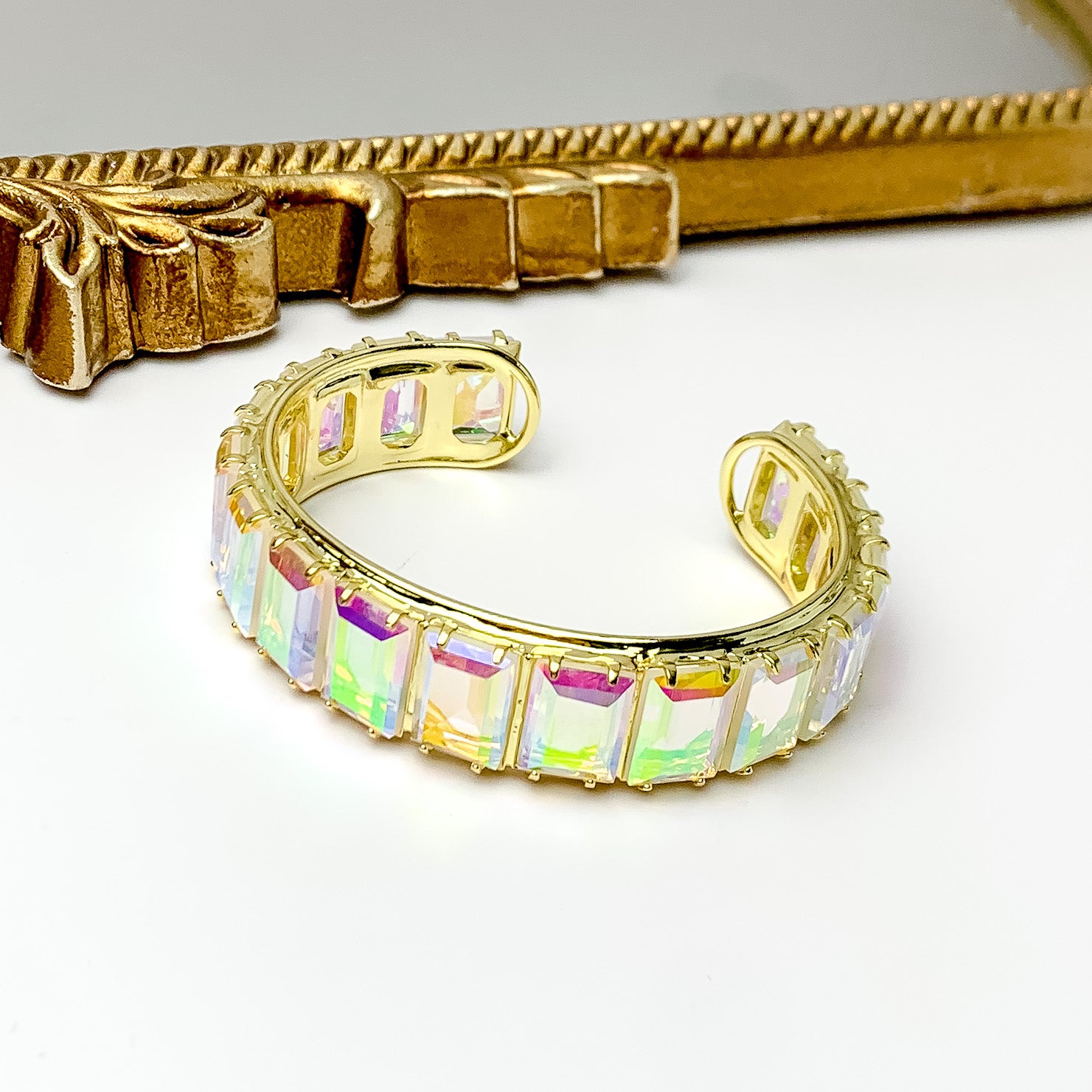 Gold bangle with a ab, rectangle crystal inlay. This bracelet is pictured on a white background with a gold mirror at the top of the picture.  