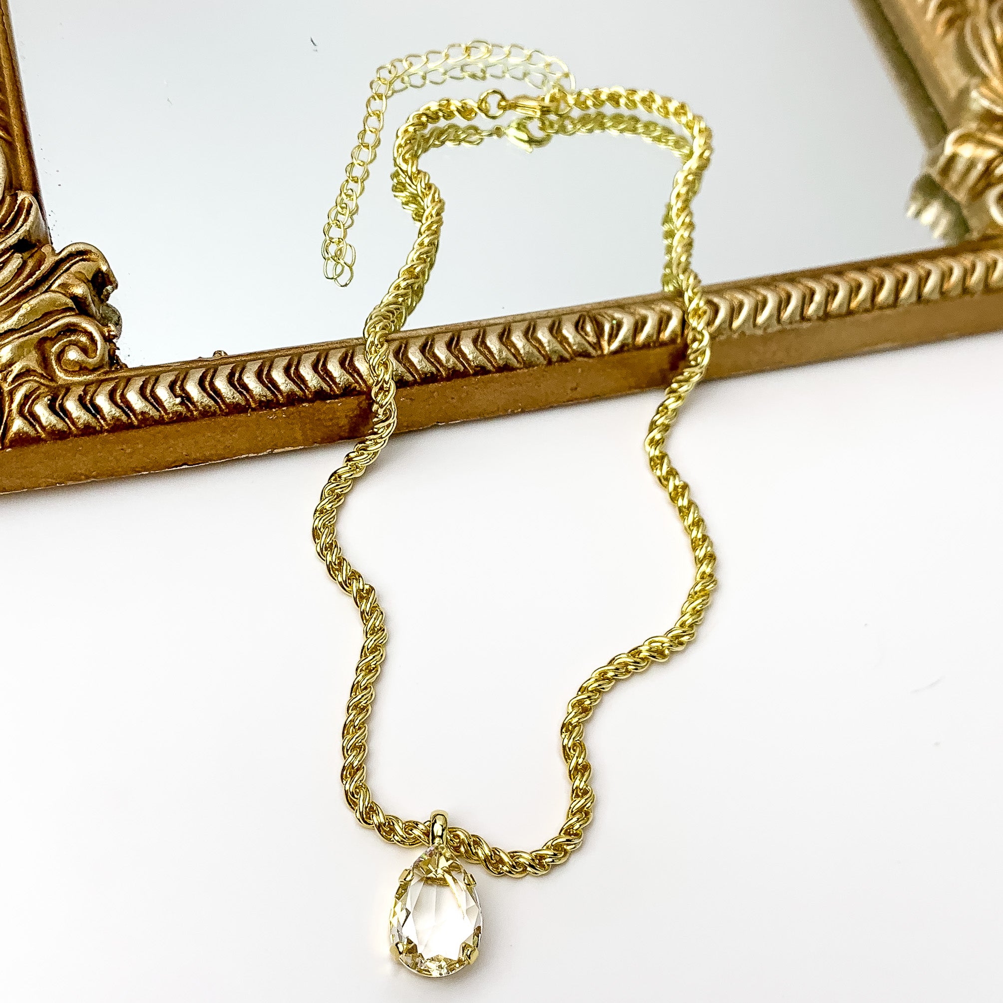 Gold necklace with clear crystal pendant in the middle. Pictured on a white background with a mirror at the top.