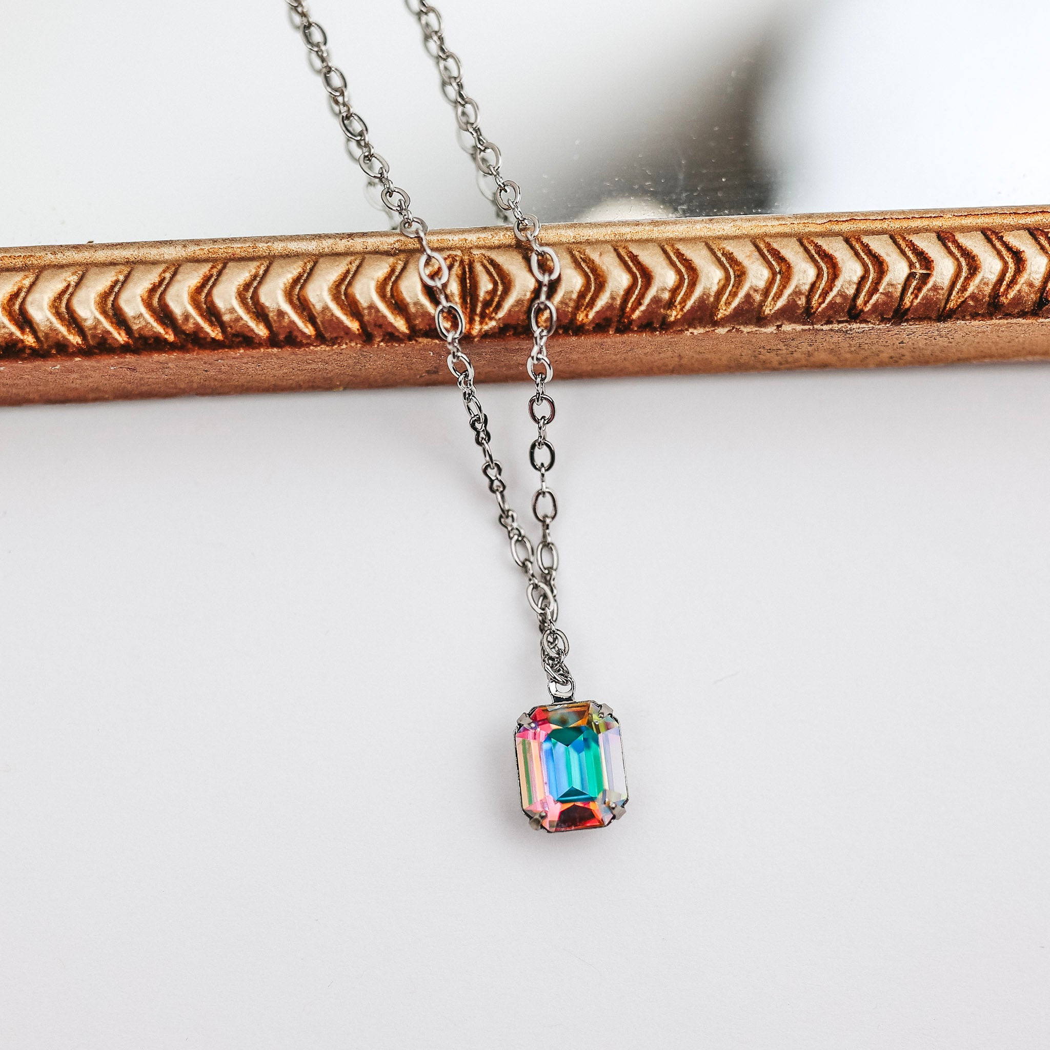 A silver-tone necklace with a single emerald cut crystal pendant that is colorful.