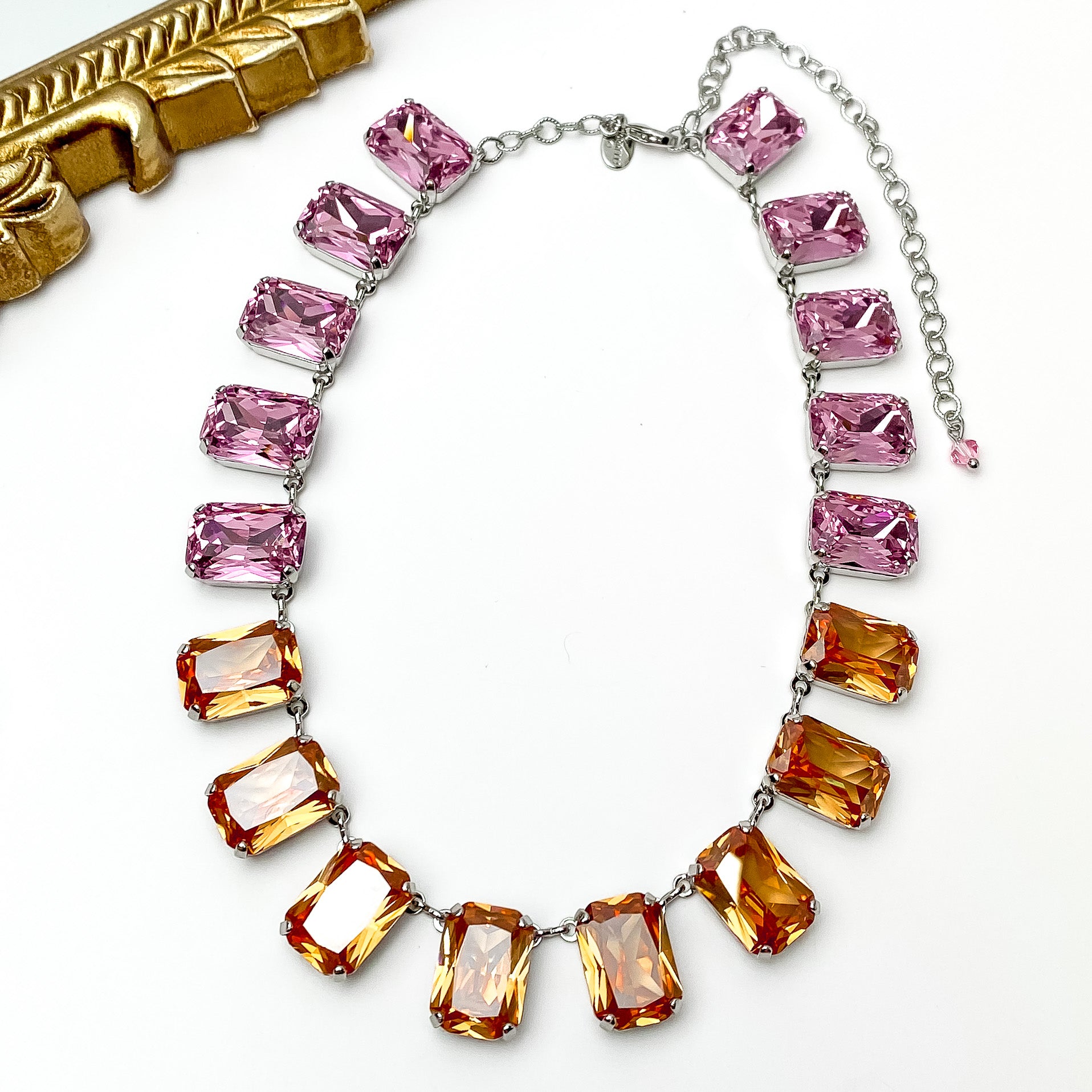 Pink and orange rectangle crystal necklace. This necklace has a silver setting. This necklace is pictured on a white background with a gold mirror in the top left corner.   
