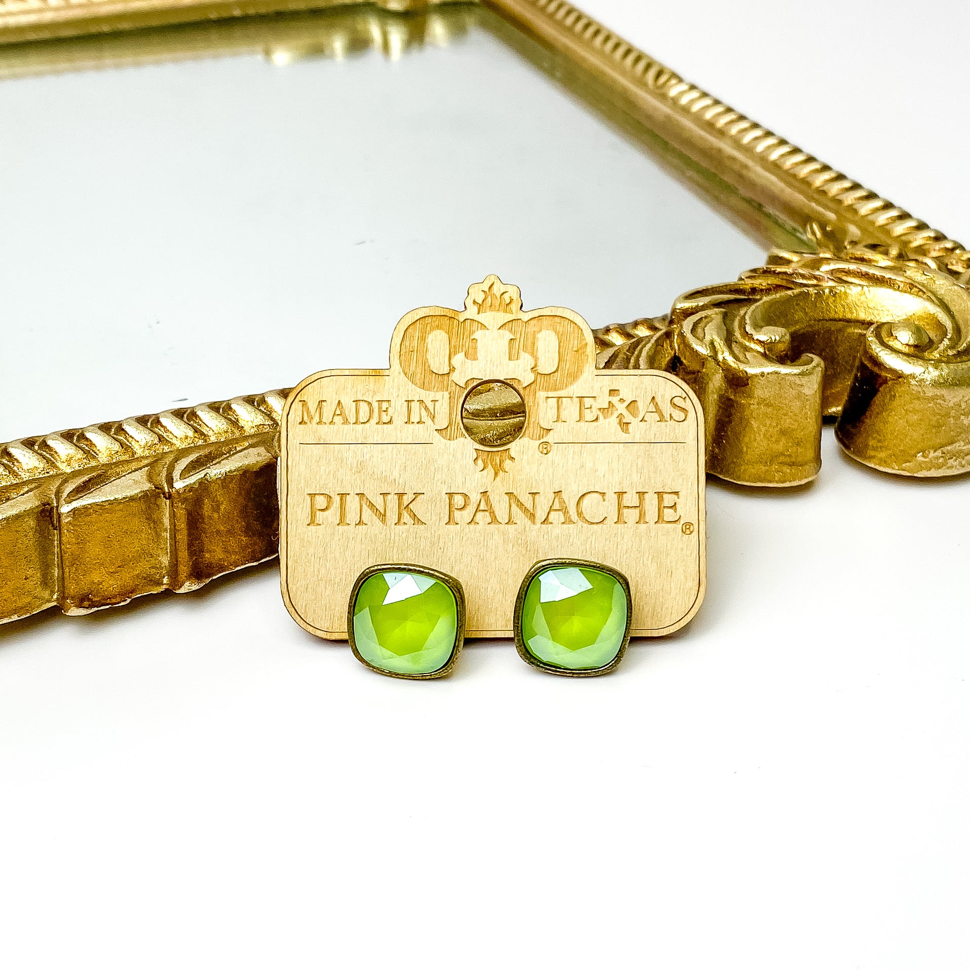 Lime green cushion cut crystal stud earrings with a bronze setting. These earrings are pictured on a Pink Panache wood holder in front of a gold mirror and on a white background. 