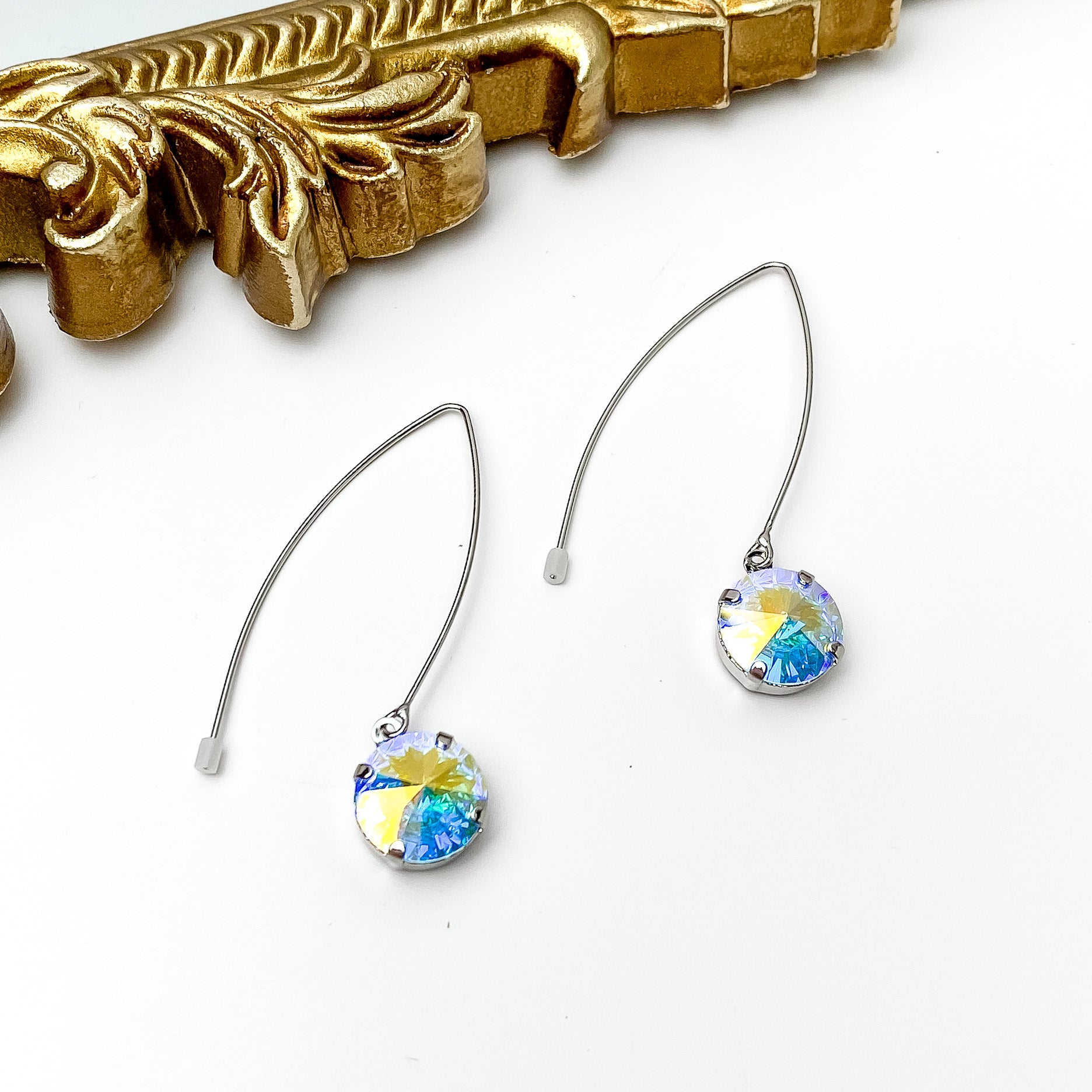 Silver, kidney wire dangle earrings. These earrings include a round ab crystal drop. These earrings are pictured in front of a gold mirror on a white background. 