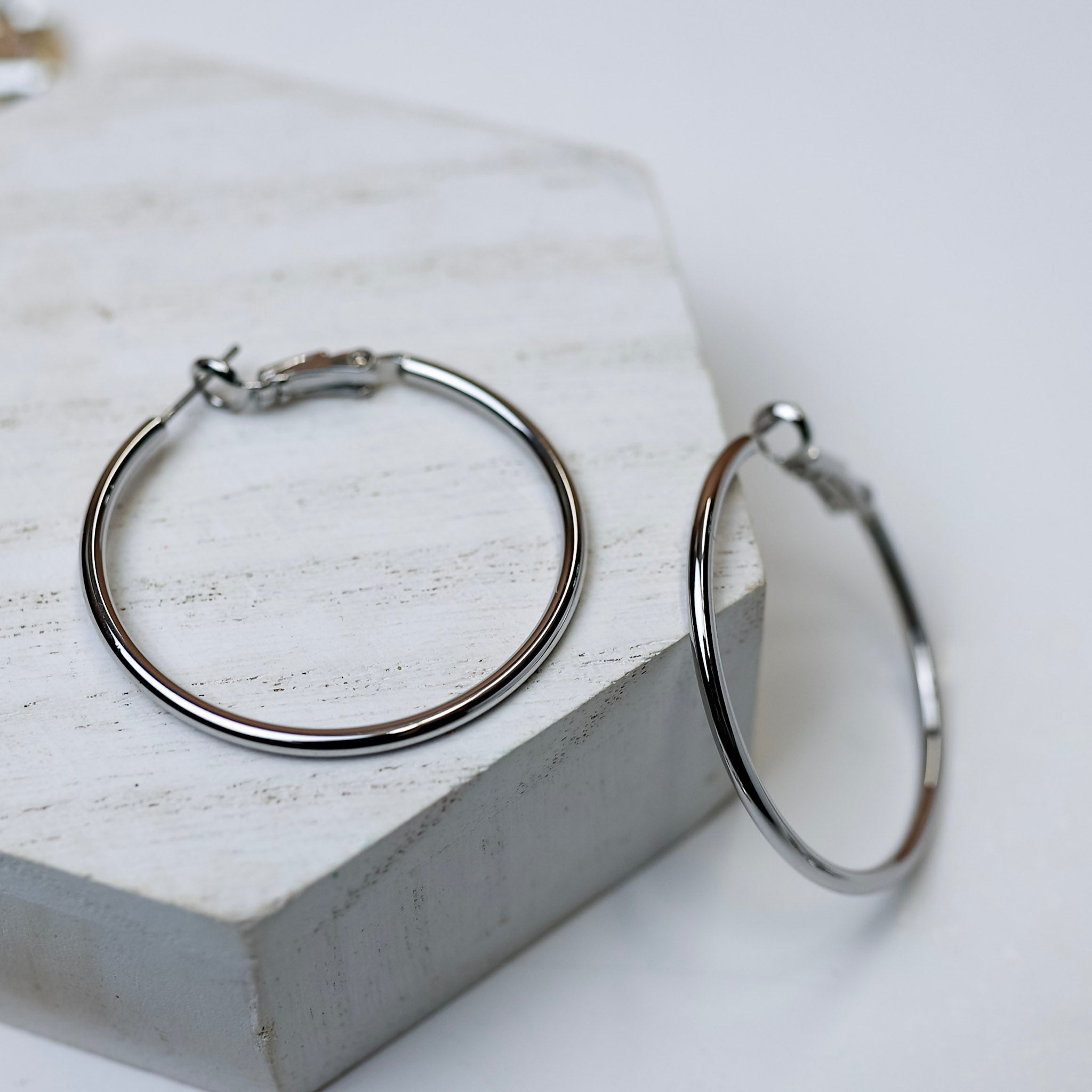 A pair of silver-tone circle hoop earrings pictured on a white background with crystal necklaces.