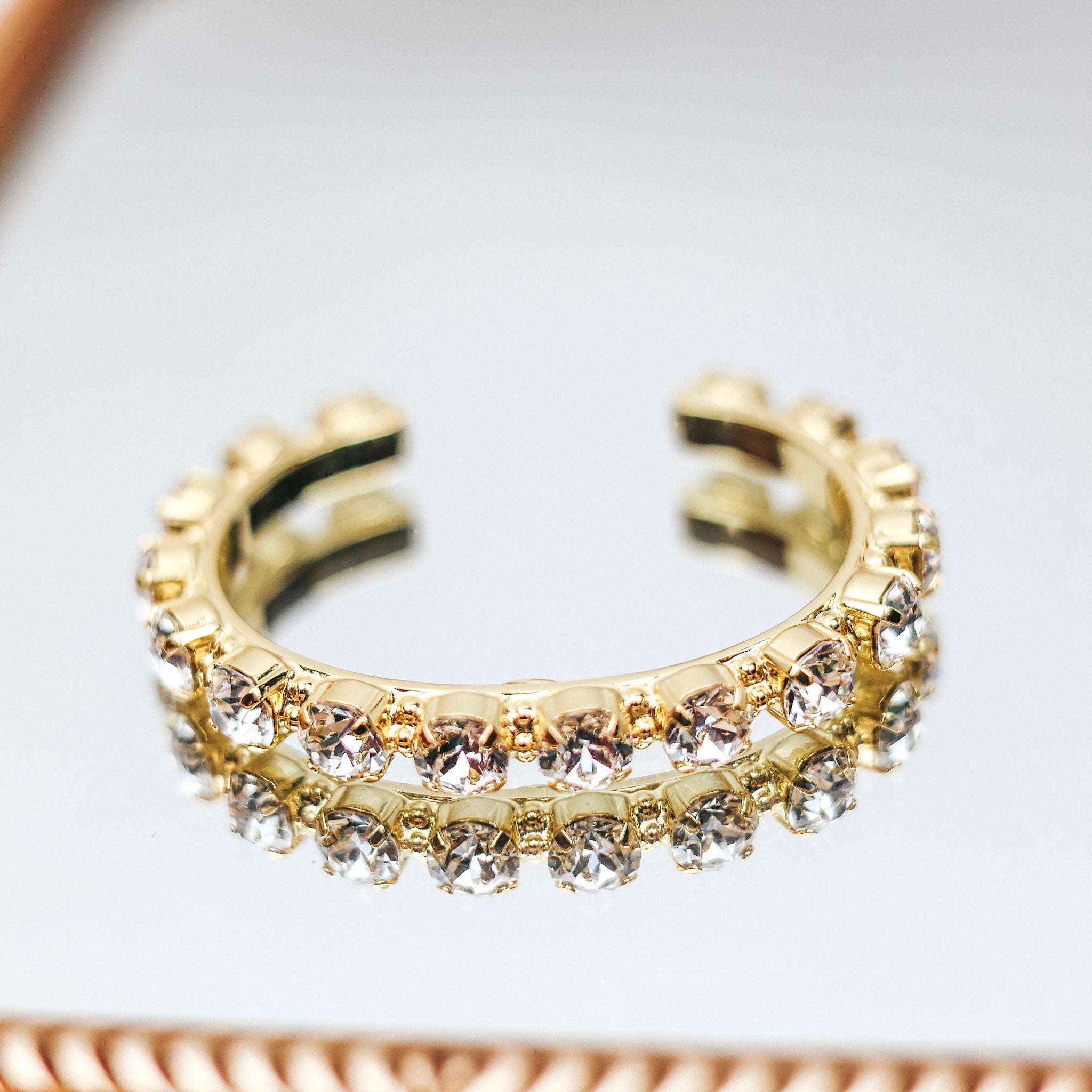 A gold tone cuff bracelet with clear crystals along the cuff.