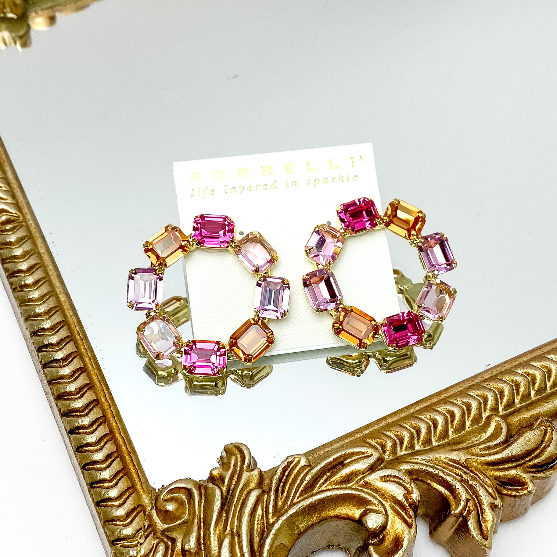 Eight rectangle crystals in pink mix in the shape of an octagon post back earrings. These earrings have a gold setting and gold prongs to hold the crystals in place. These earrings are pictured on a gold mirror on a white background. 