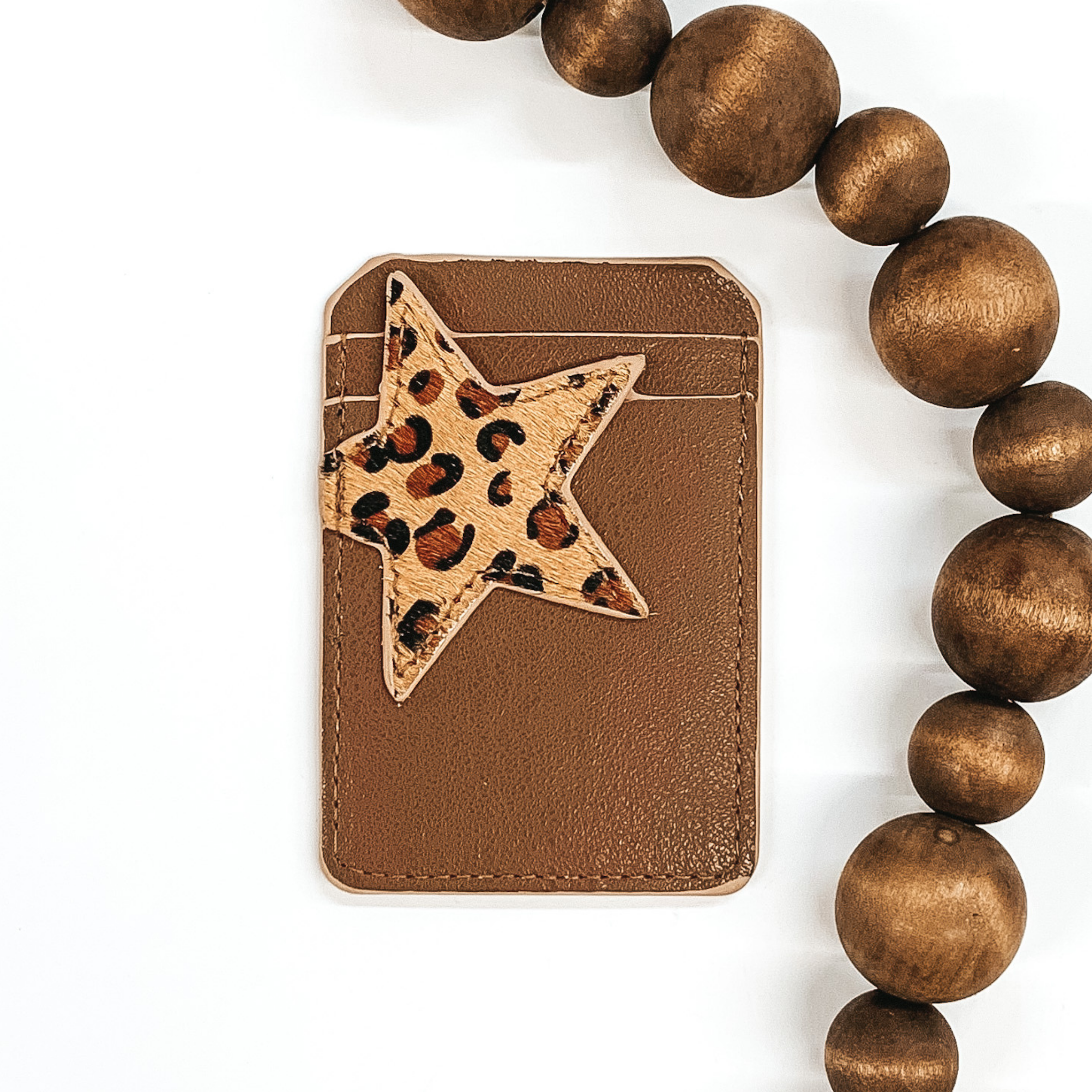 Brown card holder with two pockets that has a beige star with a leopard print on the front and can stick to the back of phones/phone cases