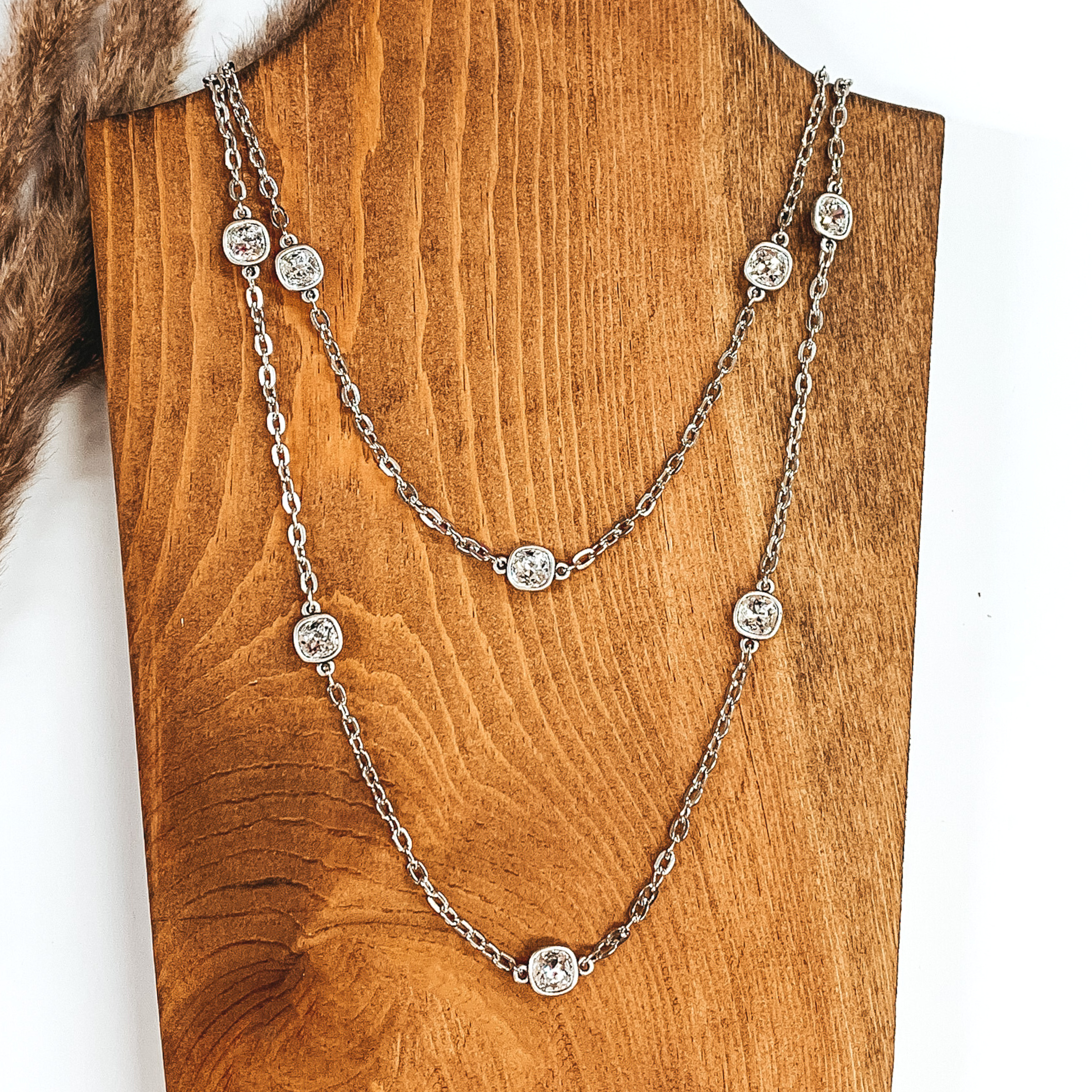 Silver chained necklace with square clear crystal spacers pictured on a wood and white background. 