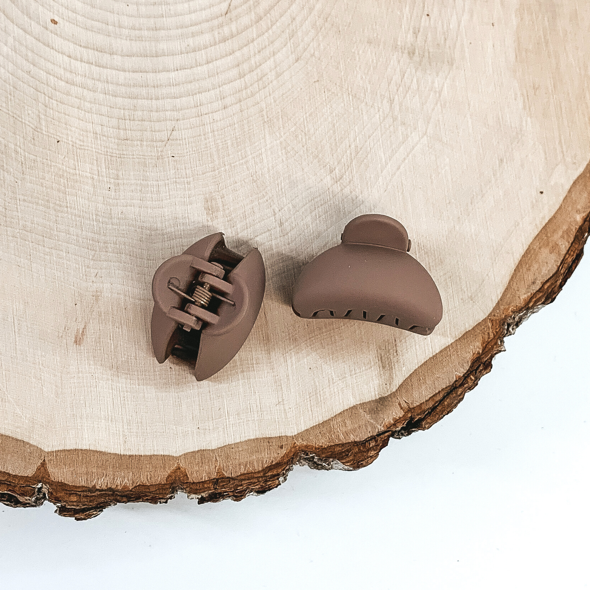 Matte taupe oval claw clips with an oval cutout. This clip is pictured on a piece of wood on a white background.