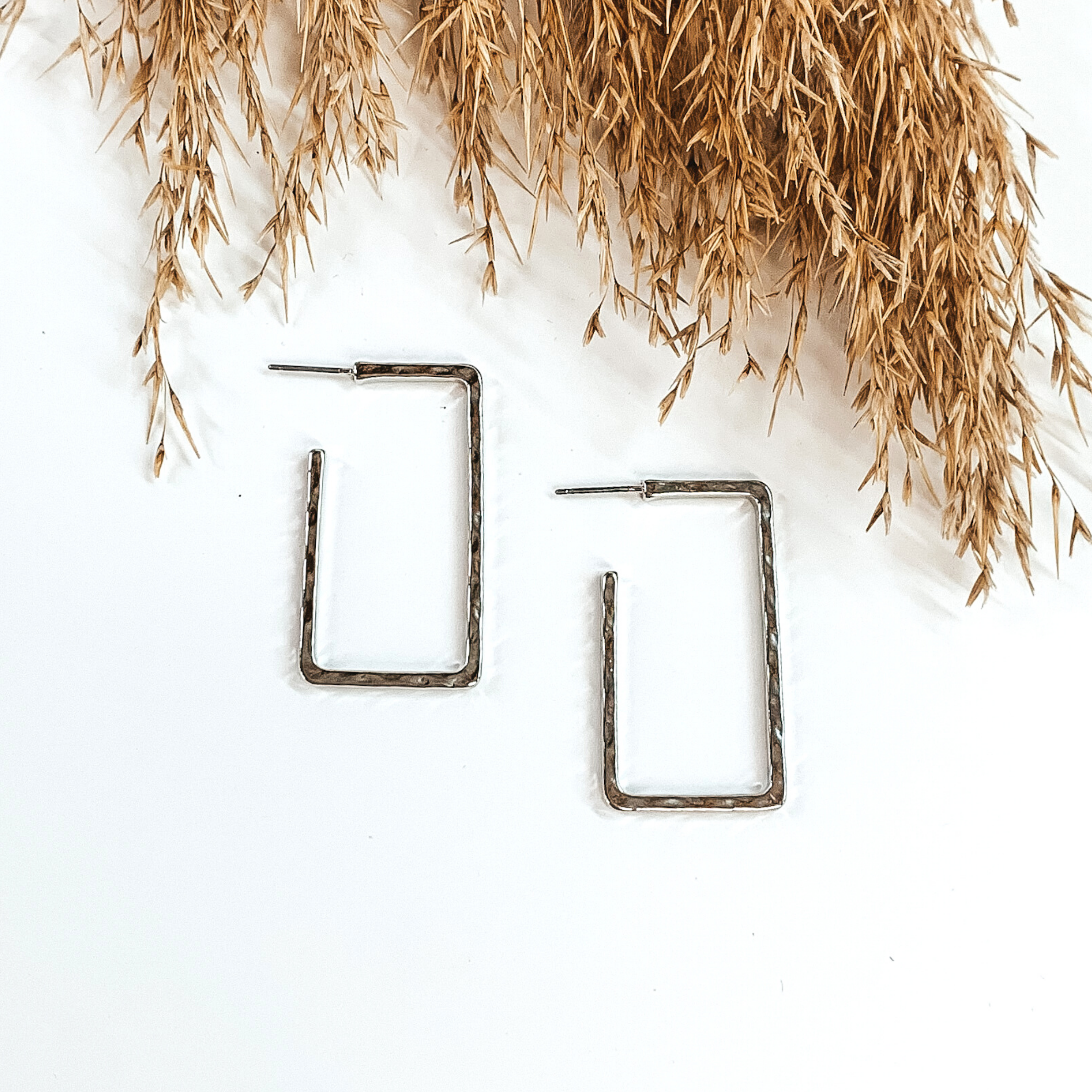 Silver rectangle hoops with a hammered look. These hoops are pictured on a white background with tan floral at the top of the picture. 