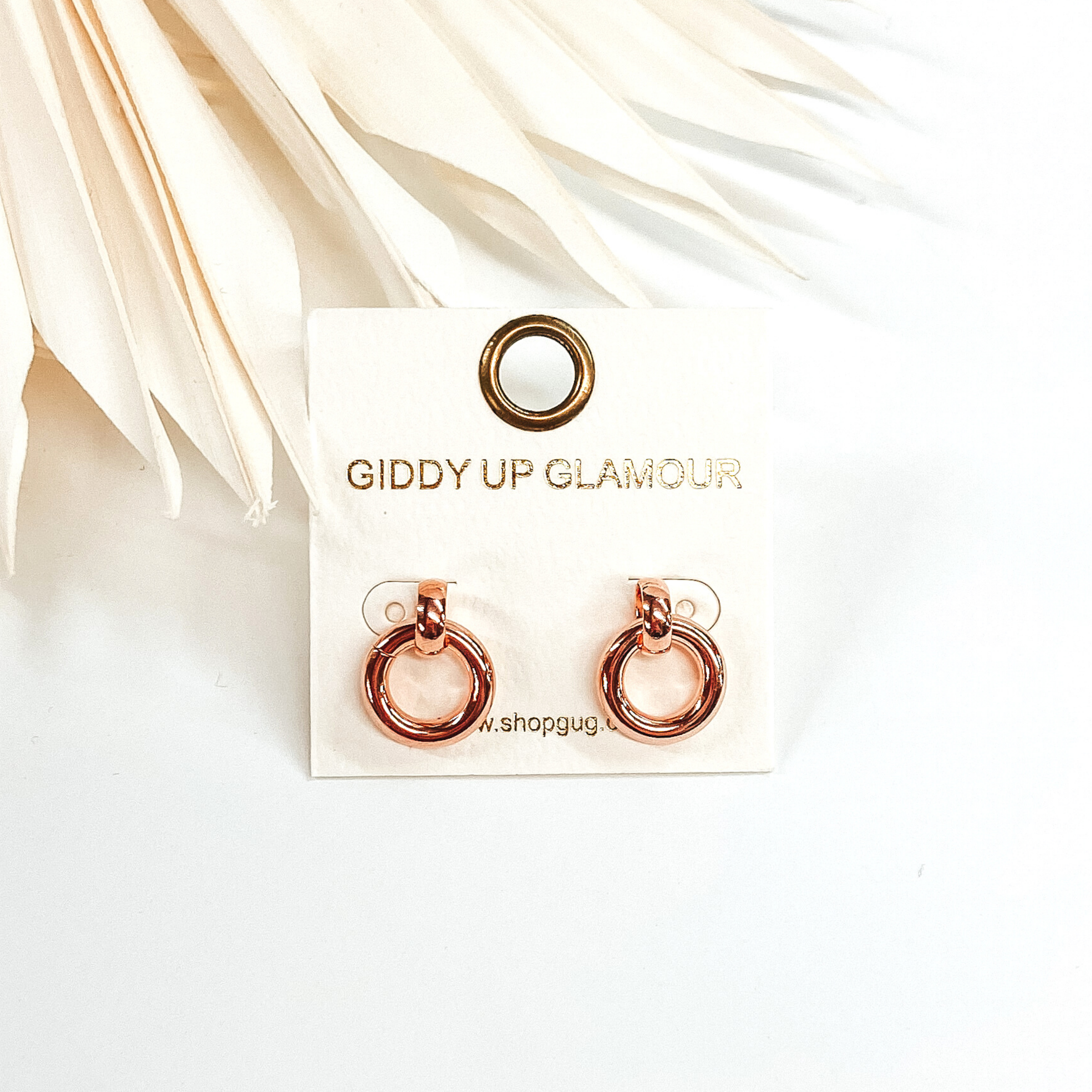 Tiny circle drop earrings in rose girl. These earrings are pictured in front of white leaves and on a white background.