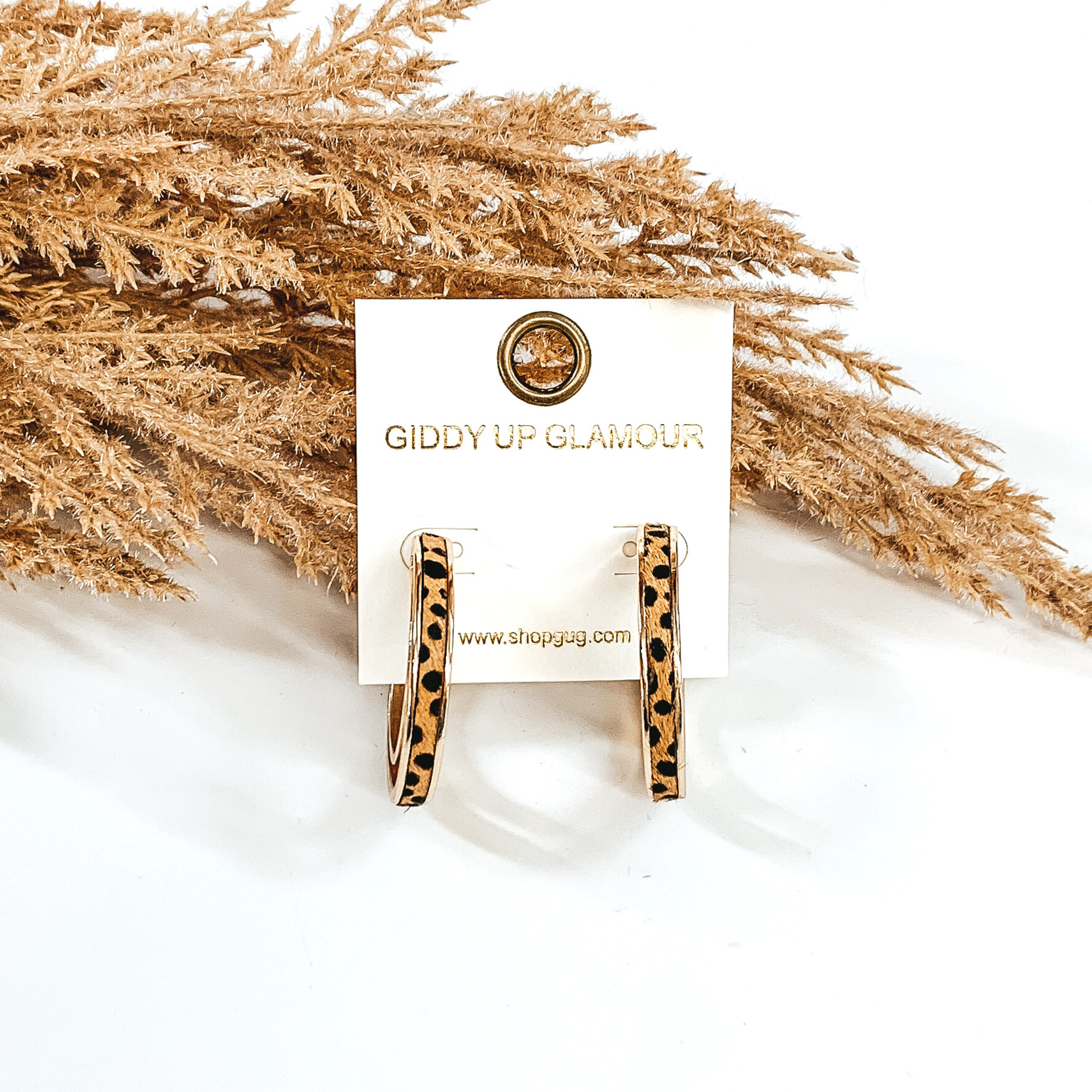 Gold hoops with brown dotted print inlay. these hoop are pictured on a white background and in front of some tan floral.