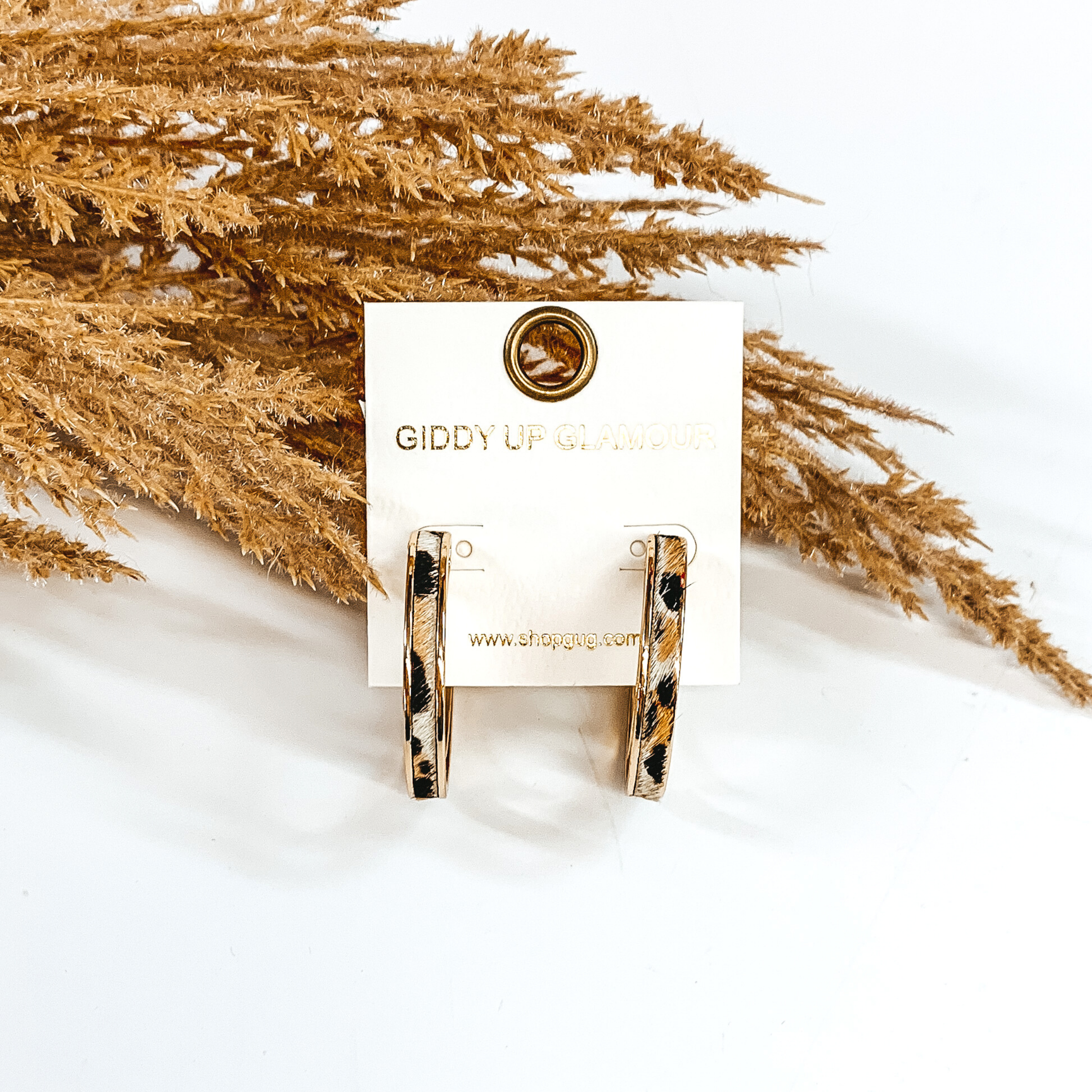 Gold hoops with white animal print inlay. these hoop are pictured on a white background and in front of some tan floral.