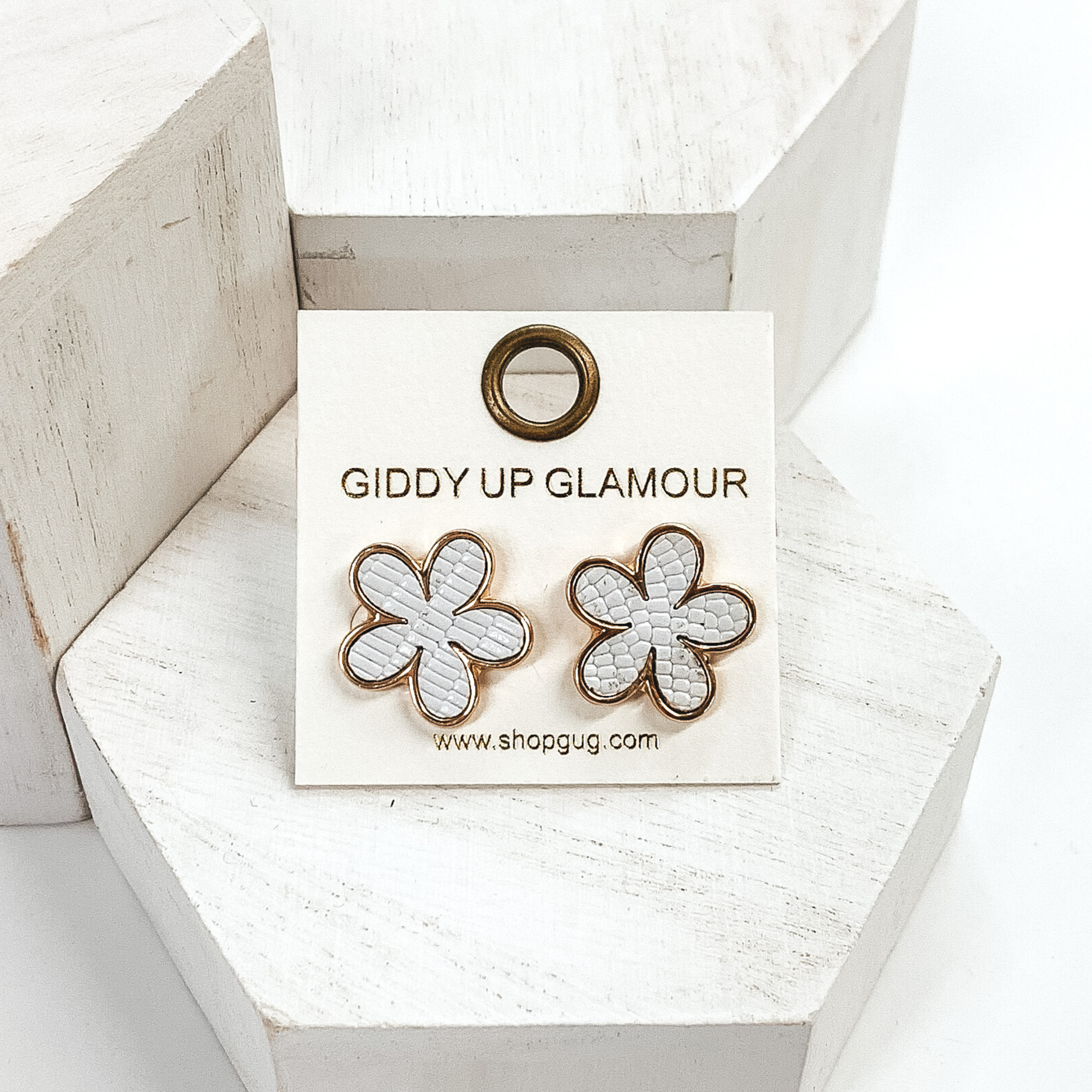 These are gold flower stud earrings with a white textured inlay. These earrings are pictured on white blocks on a white background. 