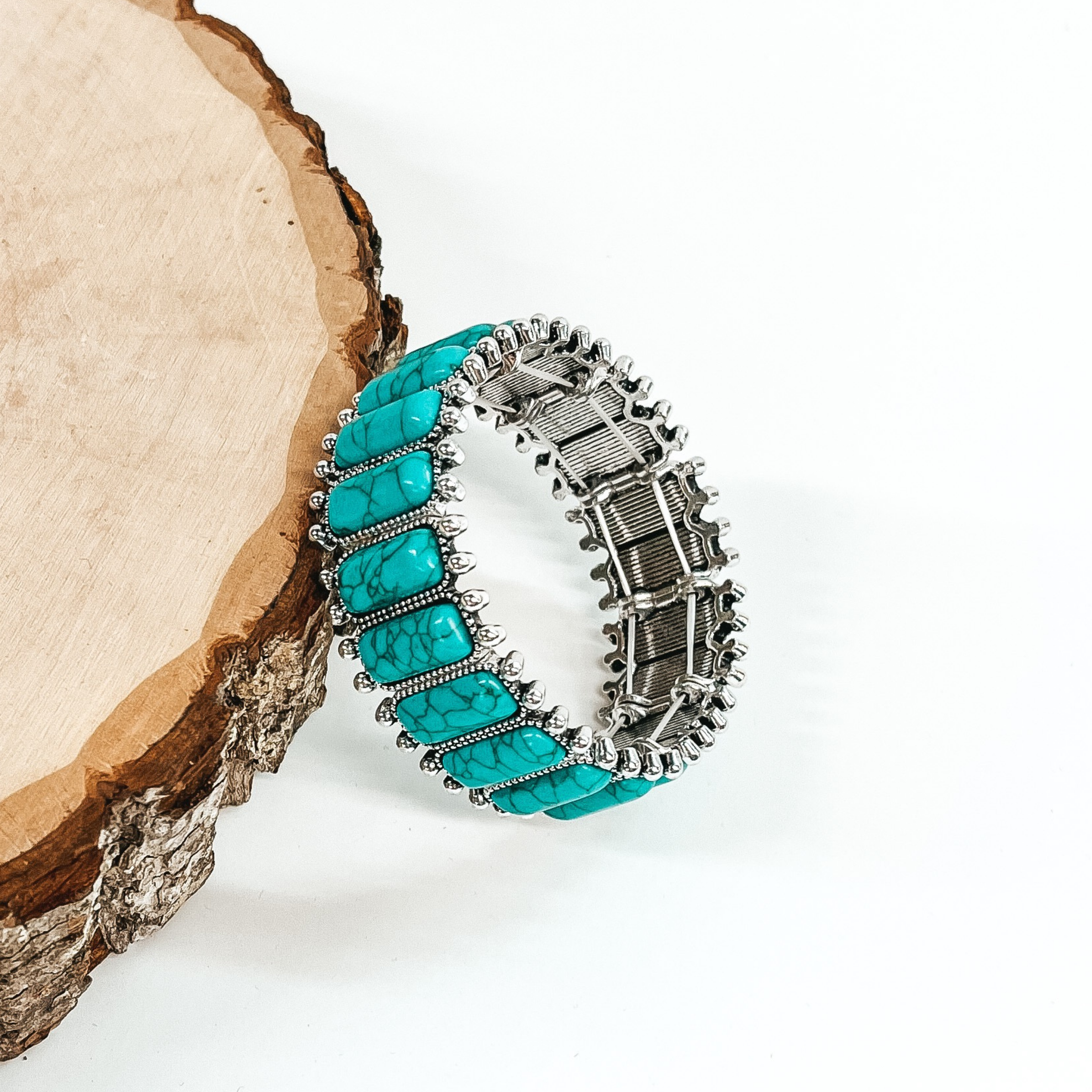Stretchy bracelet with rectangle, turquoise stone that have a silver outline. This bracelet is pictured laying against a piece of wood on a white background. 