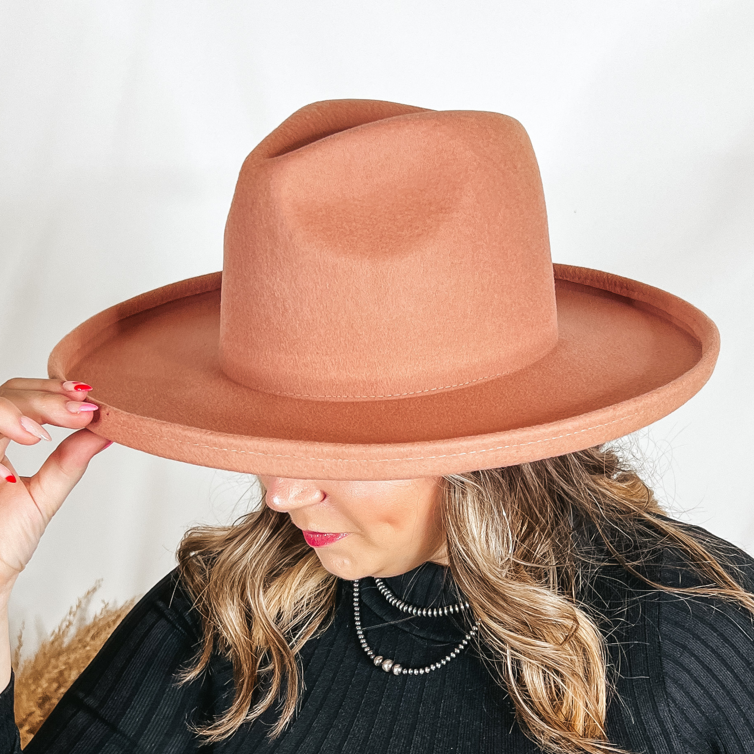 Model is wearing a coral pink rancher hat that is felt. The hat has a flat brim with a pencil roll end.