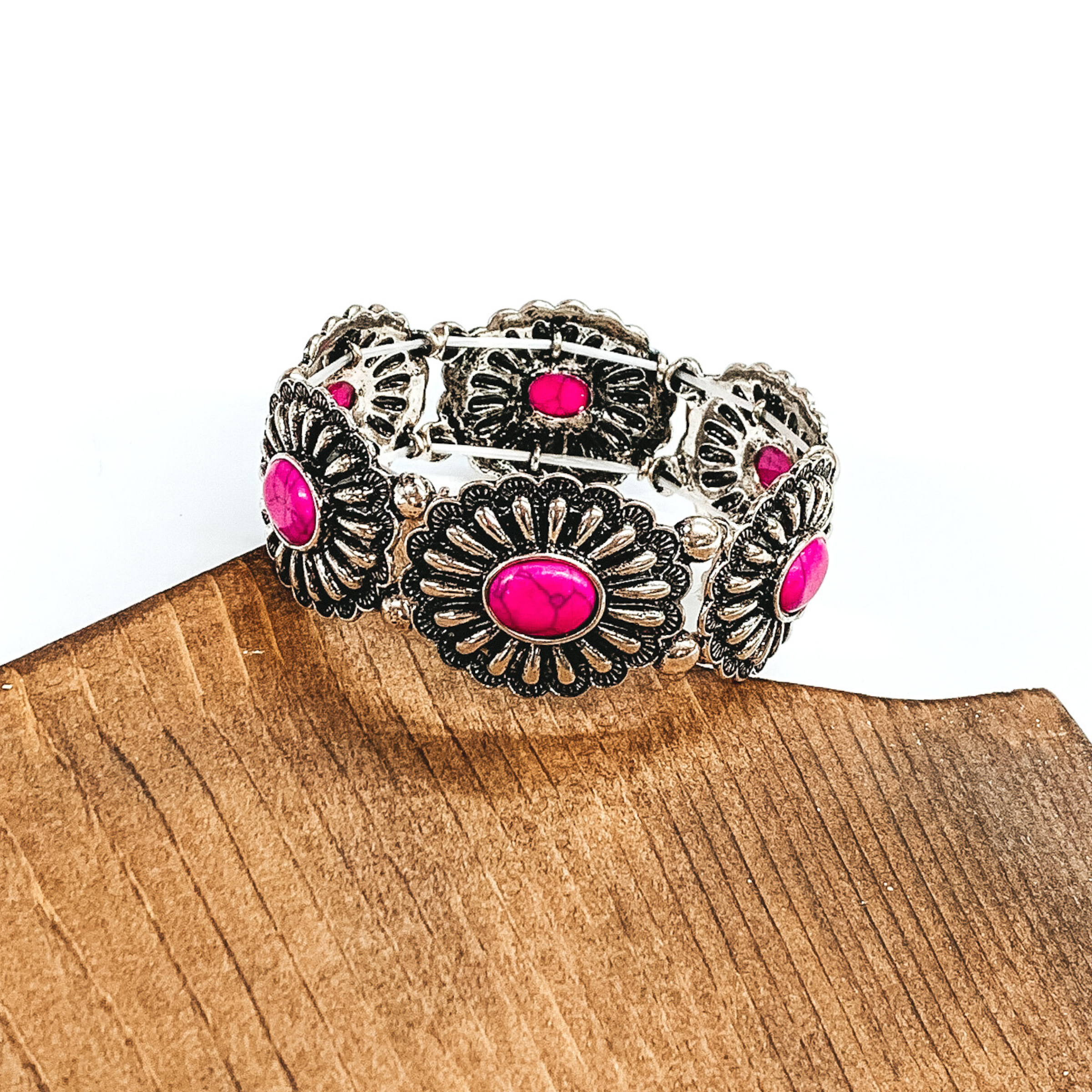 Silver, oval concho stretchy bracelet with oval center stones in pink. This bracelet is pictured partially laying on a piece of wood and on a white background.