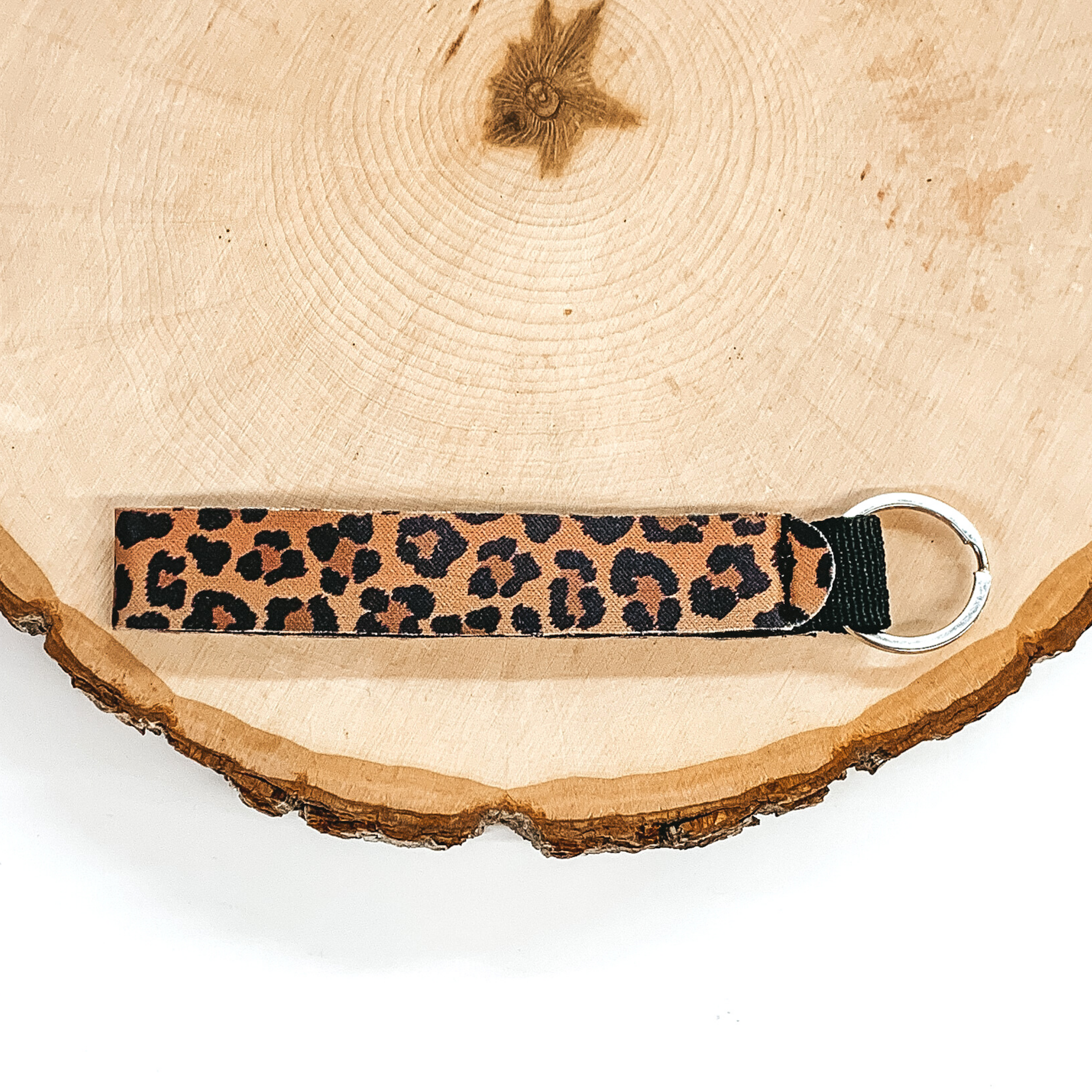 Leopard print bracelet with an attached silver key ring. This item is pictured on a piece of wood on a white background. 
