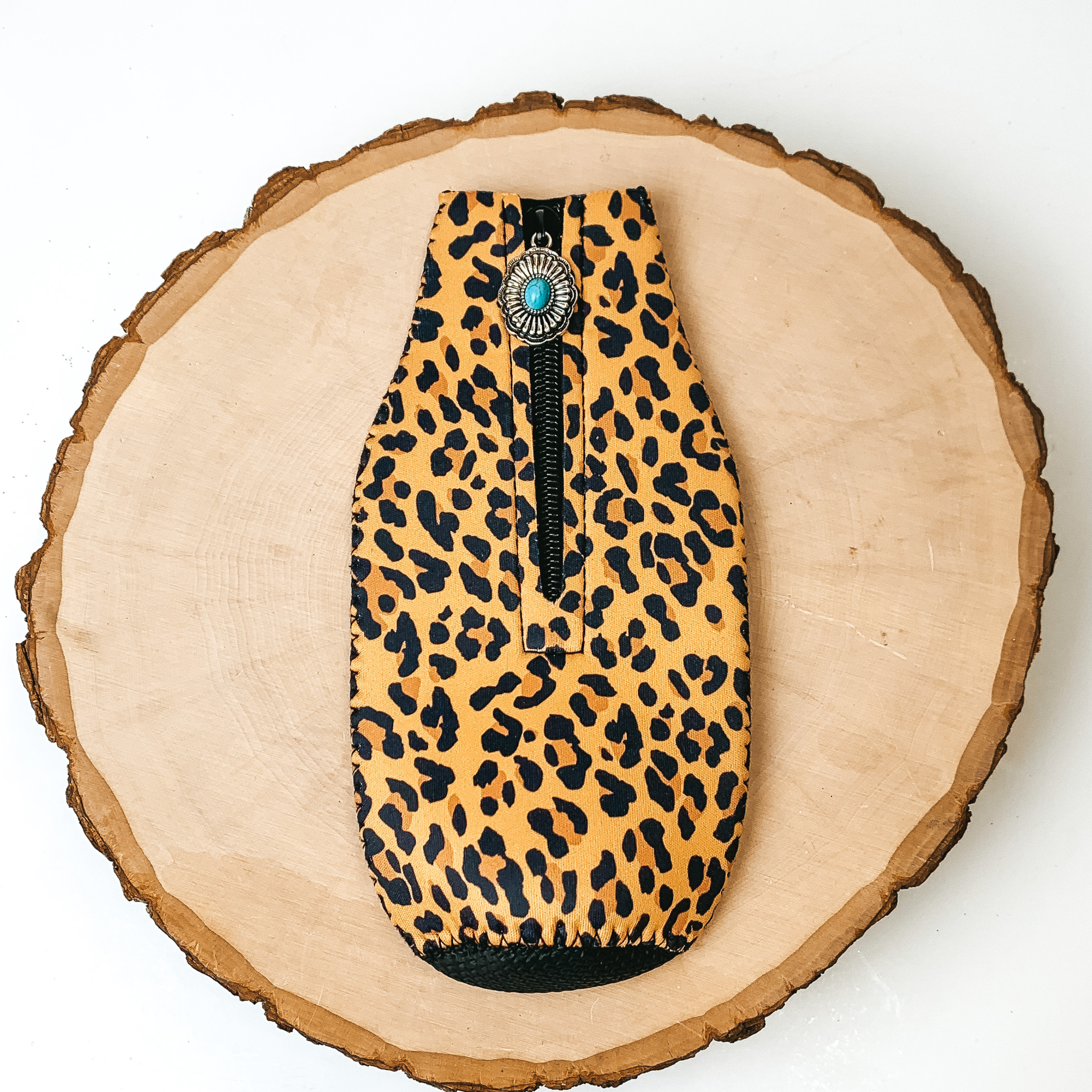 This Leopard Print Zip Up kooozie With a Concho Charm is pictured on a peice of wood, with a white background.  