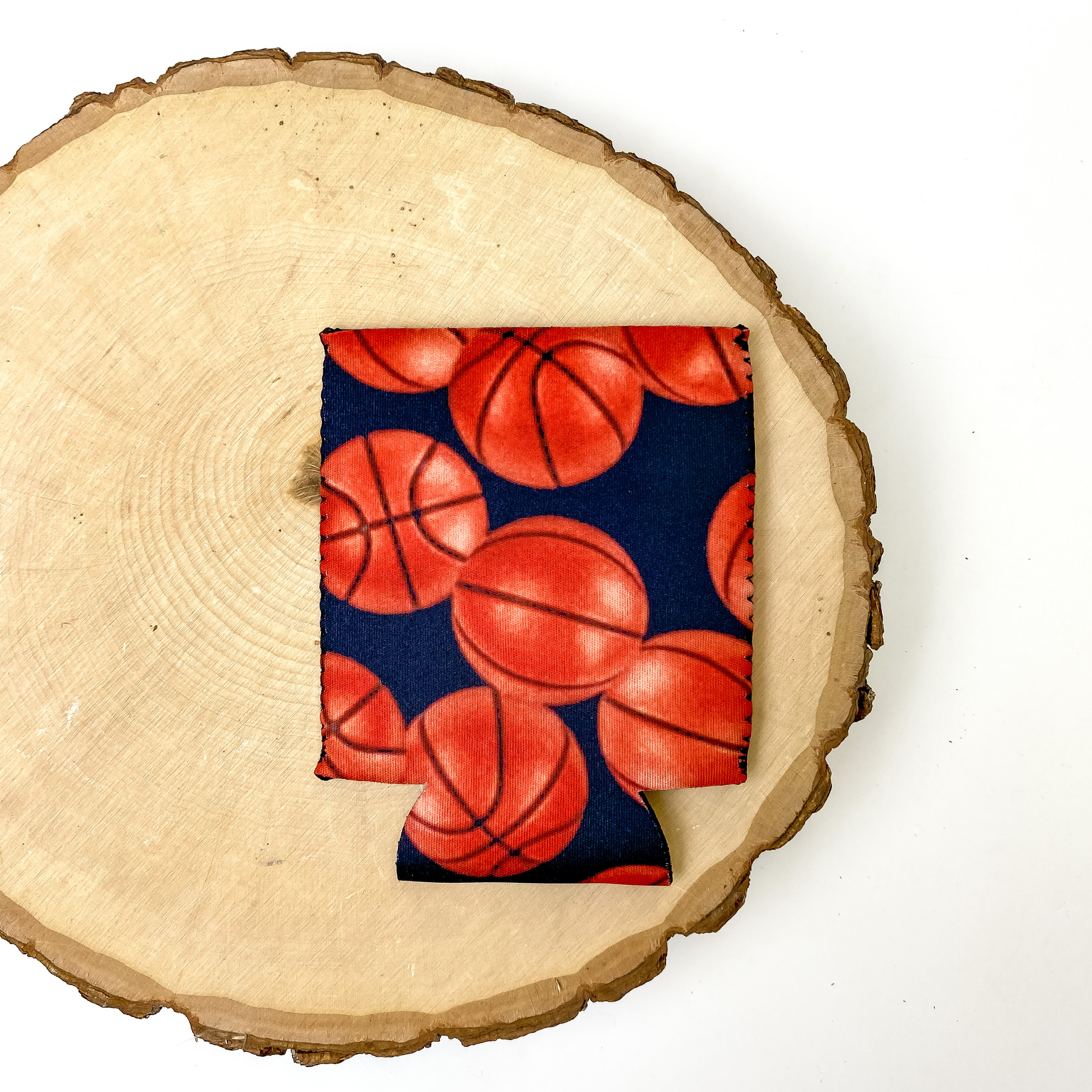 Basketball print koozie with black background. This koozie is pictured on a piece of wood on a white background.