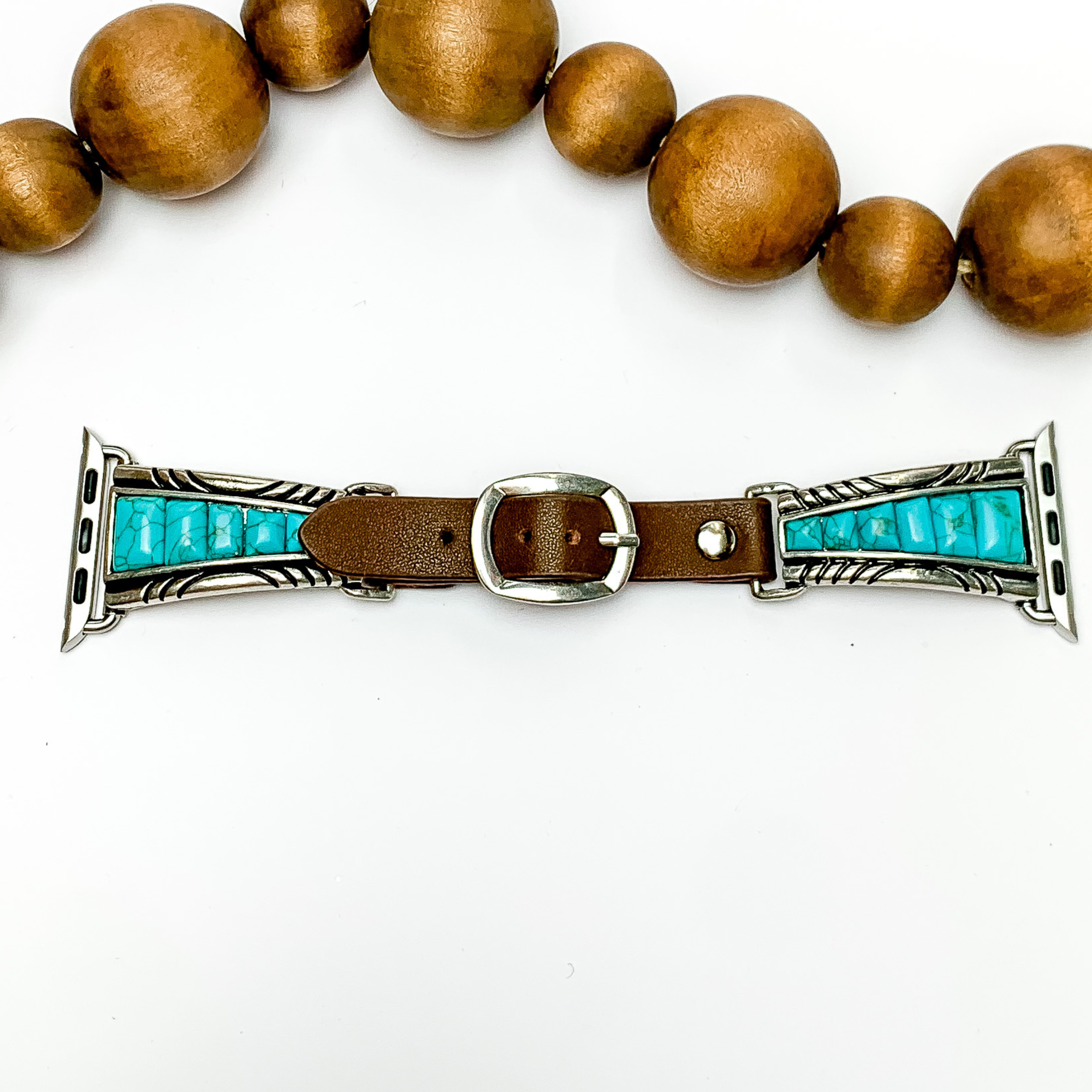 Dark Brown smart watch band with silver, five turquoise stone details going from big to small. The watch band has a western pendant with turquoise stones. This watch band is pictured on a white background with wooden beads above the watch.