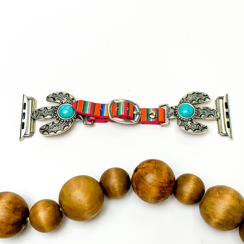 Pictured is serape apple watch band with silver cactus pendants and turquoise center stones. They are pictured with wooden beads on a white backgrounds.