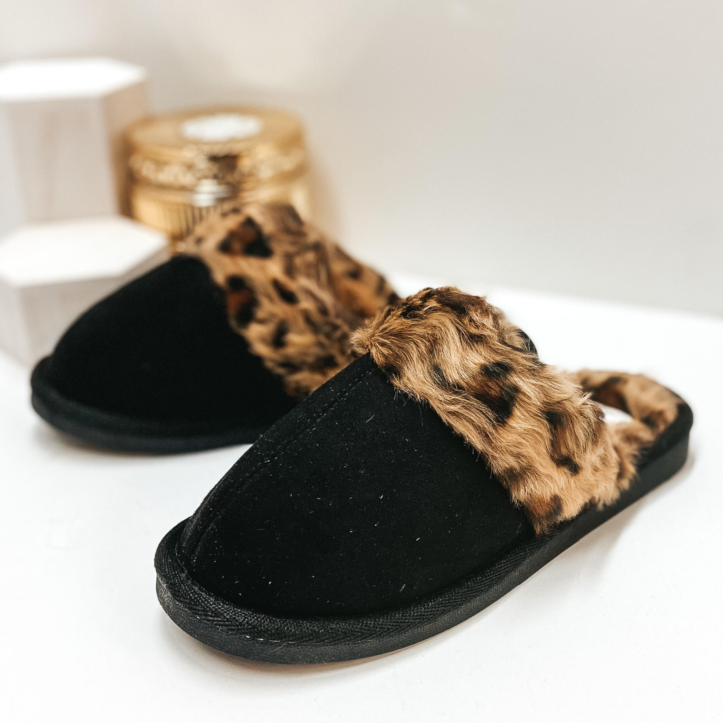 Black house slippers with leopard furry lining. Pictured on white background.