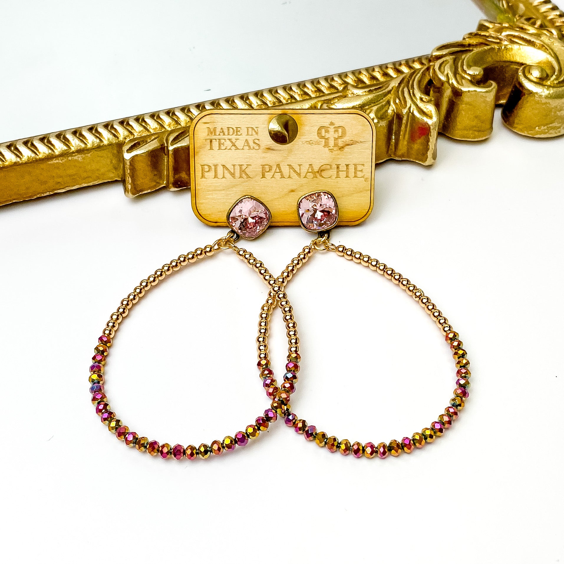 Light rose cushion cut post back earrings with a teardrop pendant. This pendant includes half gold beads and the bottom half with dark pink beads. These earrings are pictured on a wood earrings holder in front of a gold mirror on a white background. 