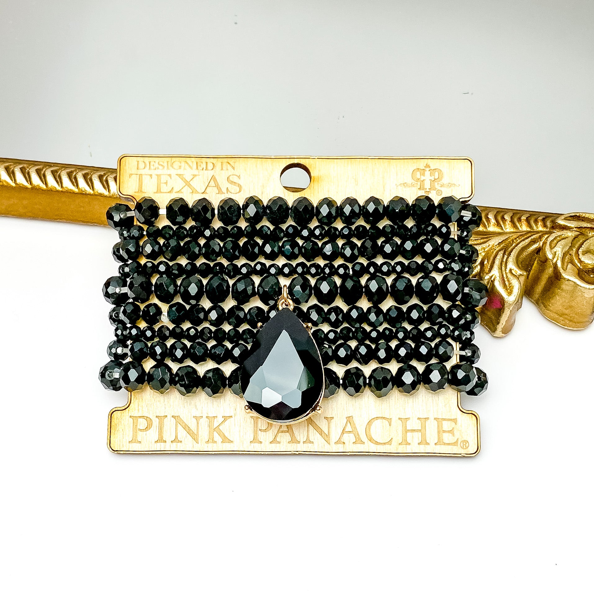 Set of nine black crystal bracelets in different sizes. One bracelet includes a large black crystal. These braceets are pictured on a Pink Panache wood holder in front of a gold mirror and on a white background. 