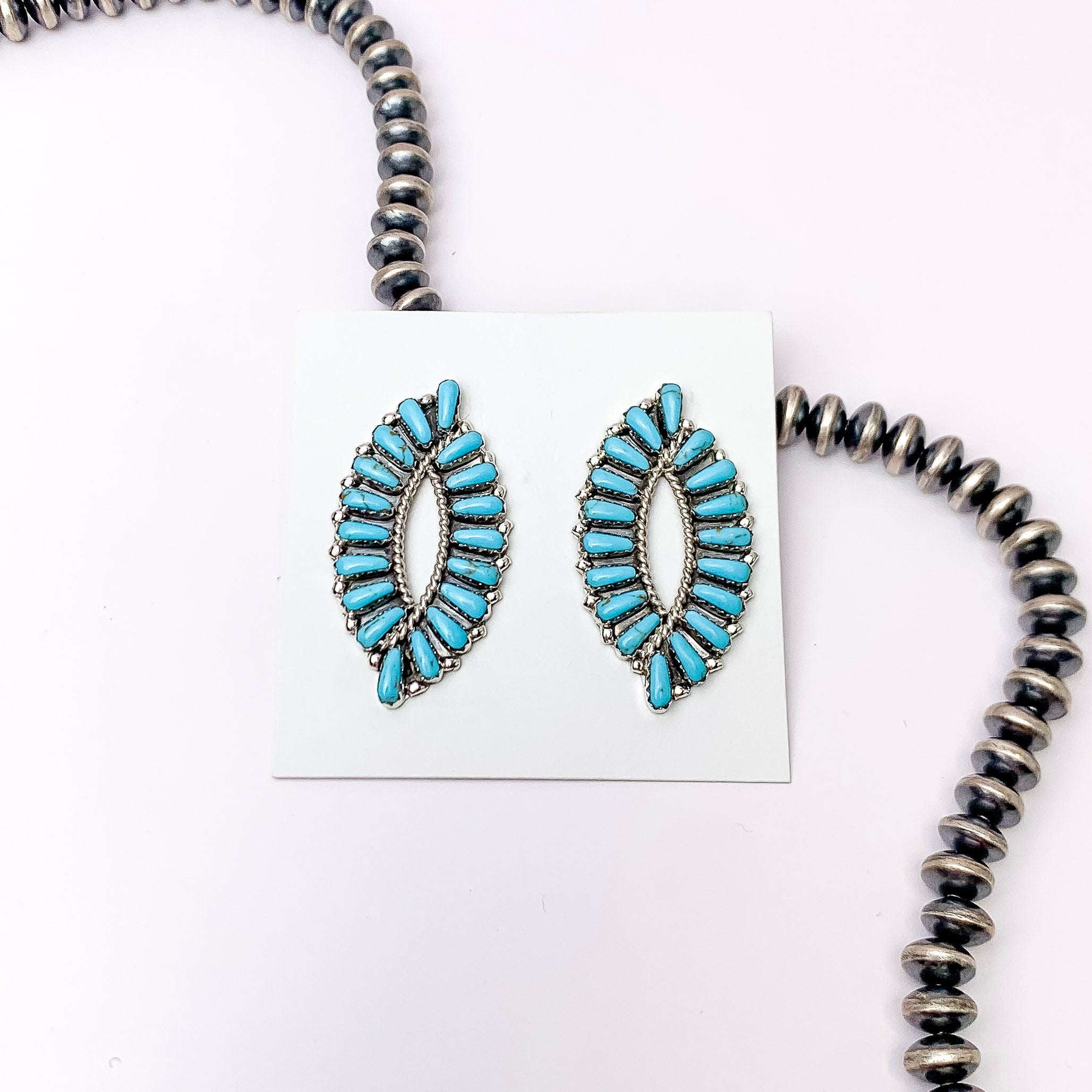 Centered in the picture is genuine turquoise cluster earrings on a white background with a strand of navajo pearls behind the earrings. 