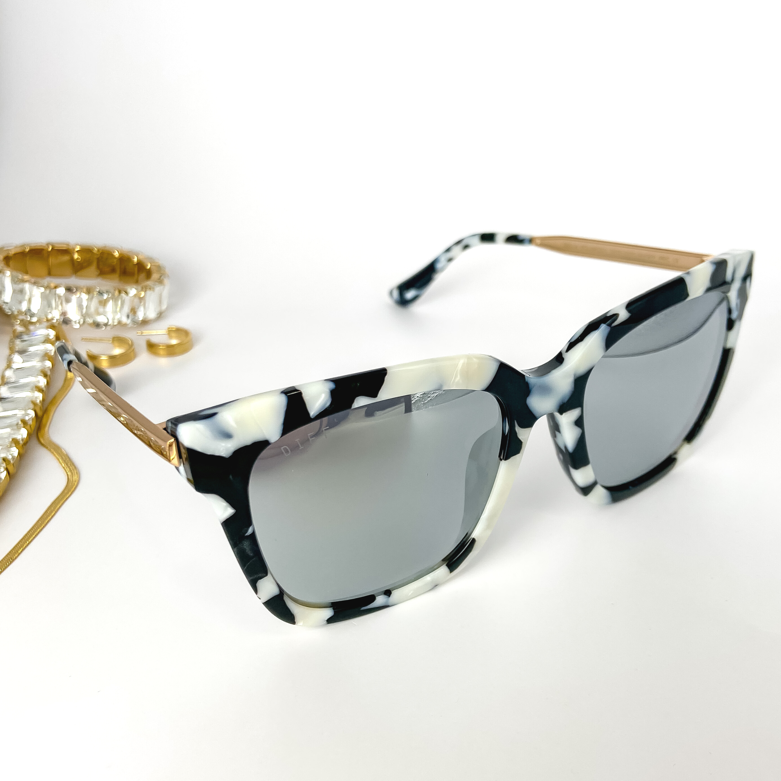 A pair of black and white print sunglasses with grey lenses and gold-tone trim. These sunglasses are pictured open on a white background with gold jewelry.