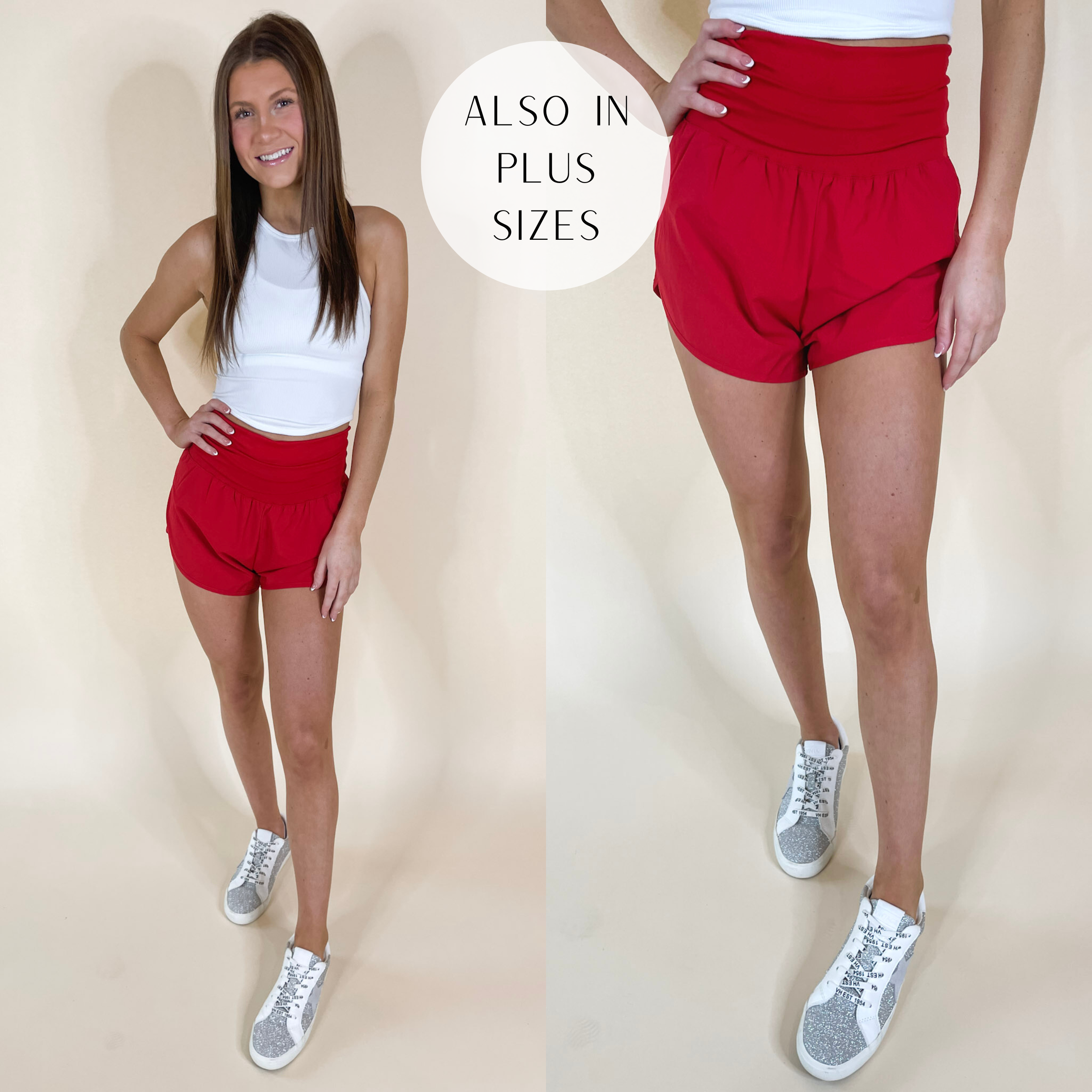 Model is wearing a pair of high waist running shorts that have a fold-over waist band. Model has these red shorts paired with white sneakers and a white tank top.