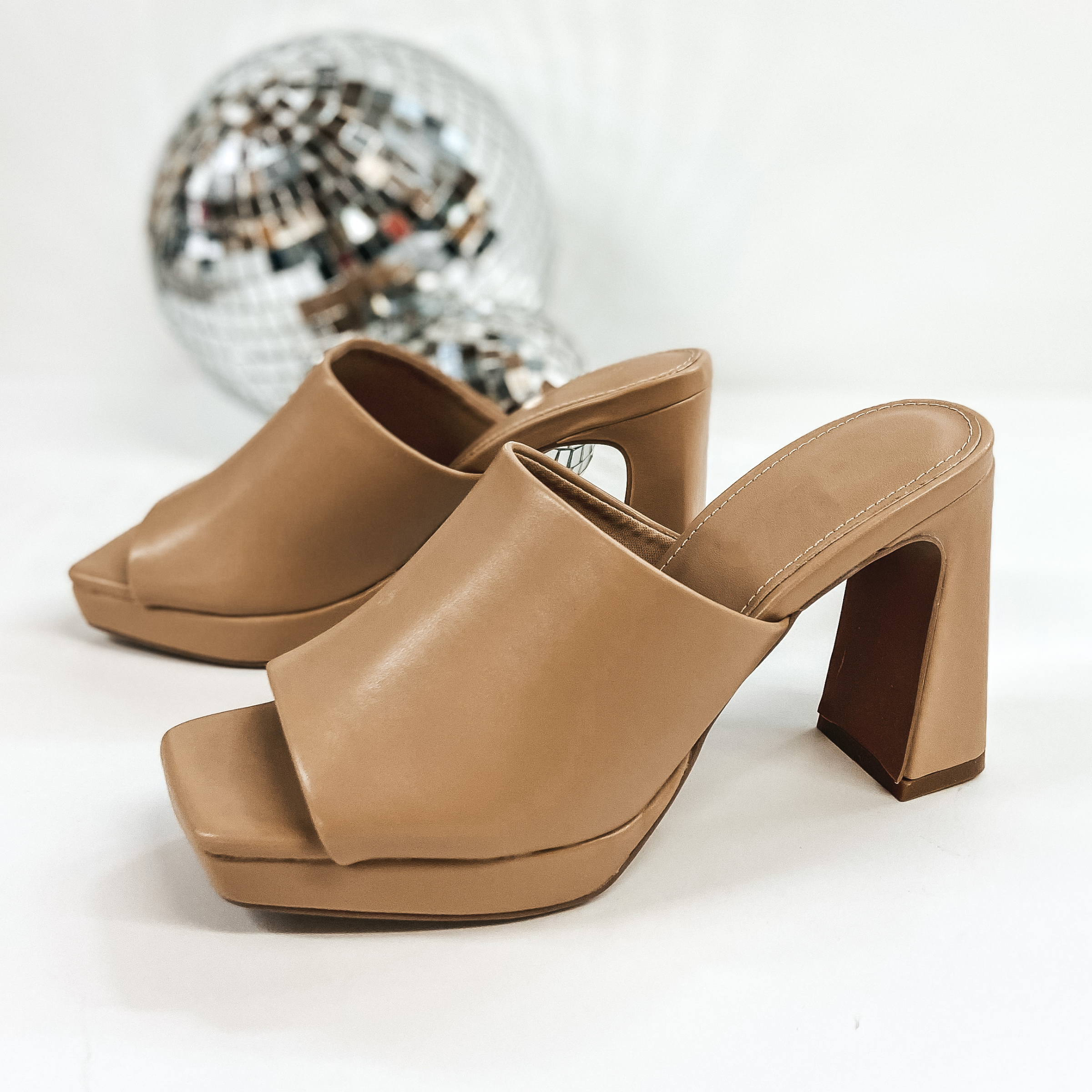 A pair of platform shoes with a slip on upper and open toe. These shoes have a high block heel. The tan heels are pictured on white background with disco balls.
