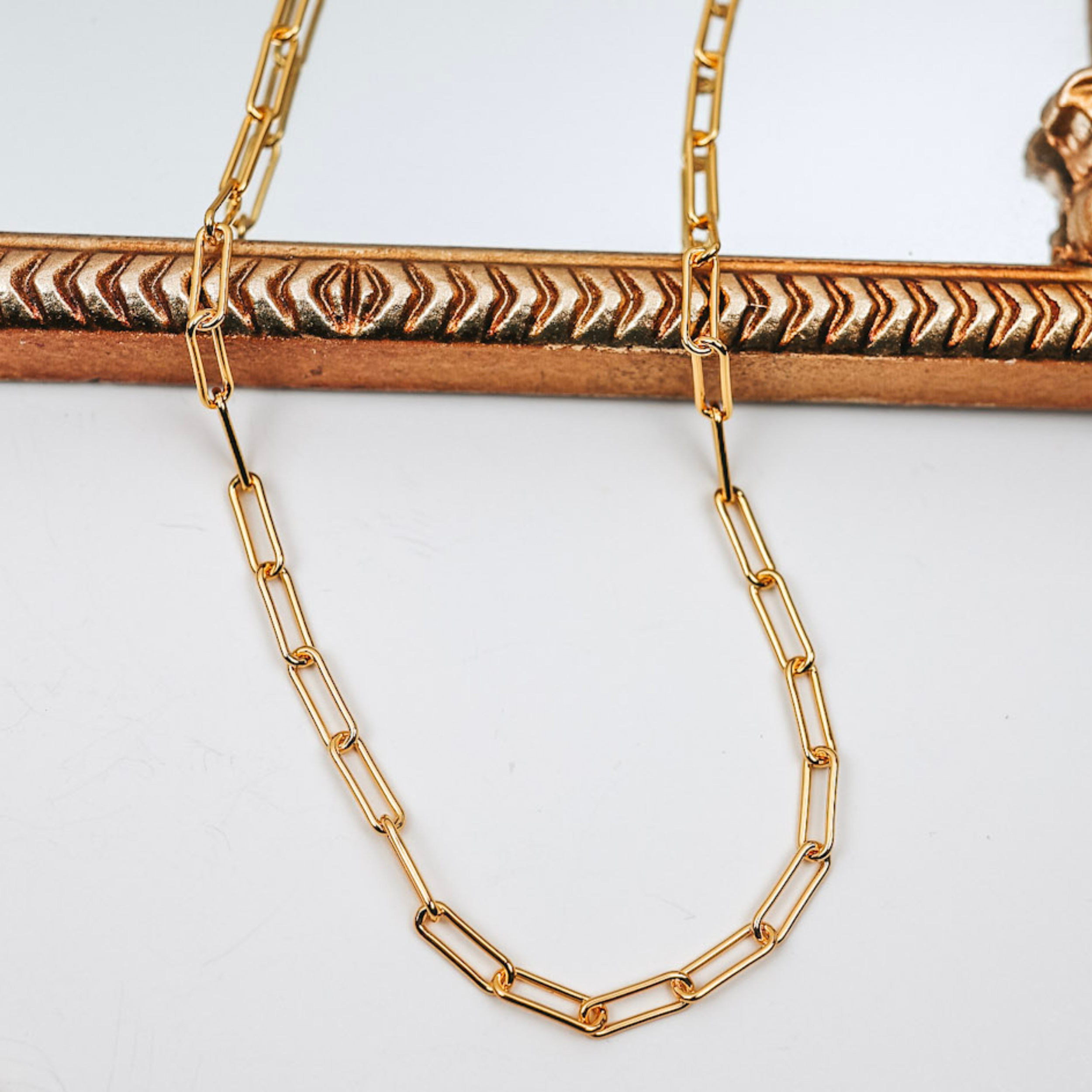 A gold-tone necklace that has paper-clip style links. This necklace is pictured on a white background with a mirror.