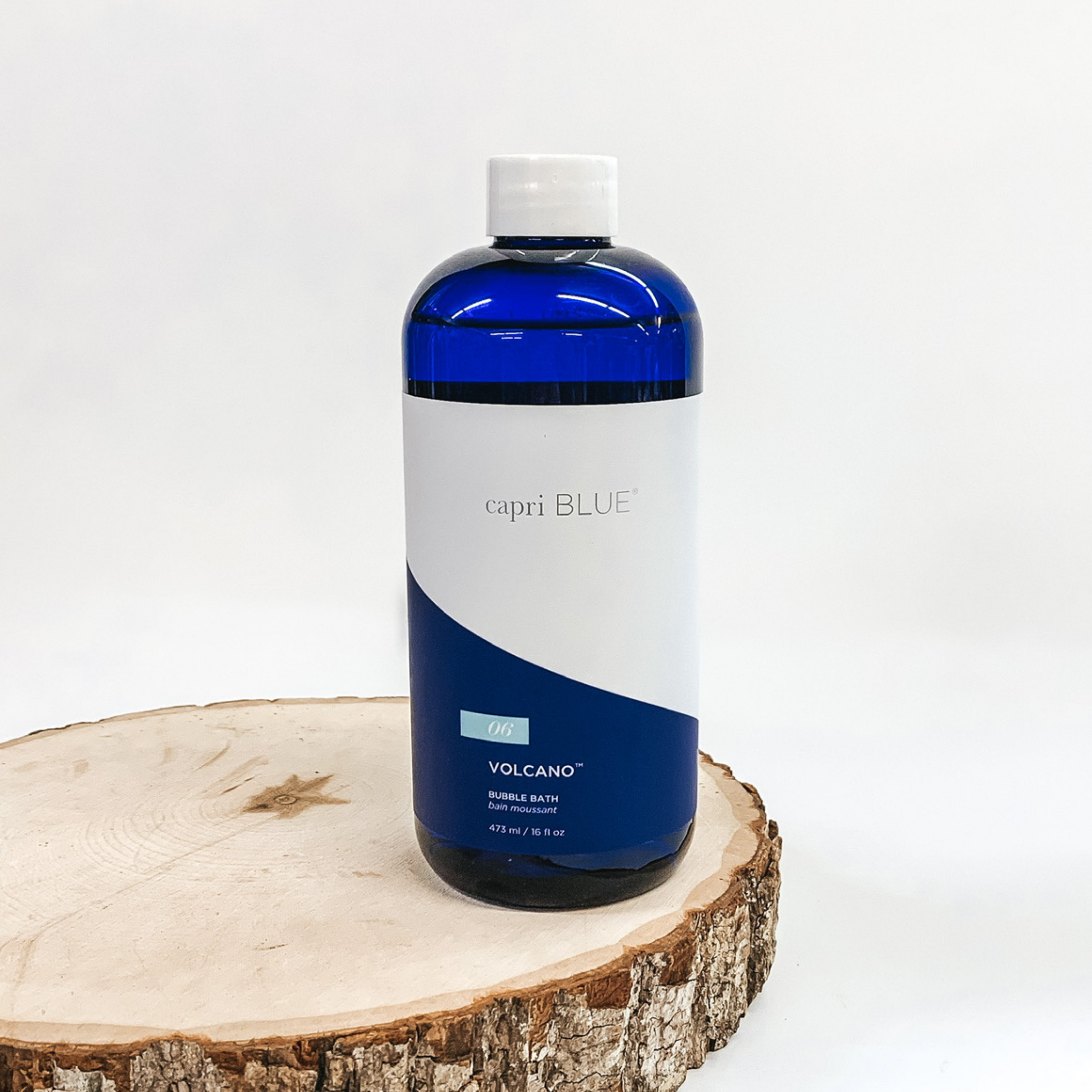 A blue bottle of bubble bath pictured on wooden display on white background.