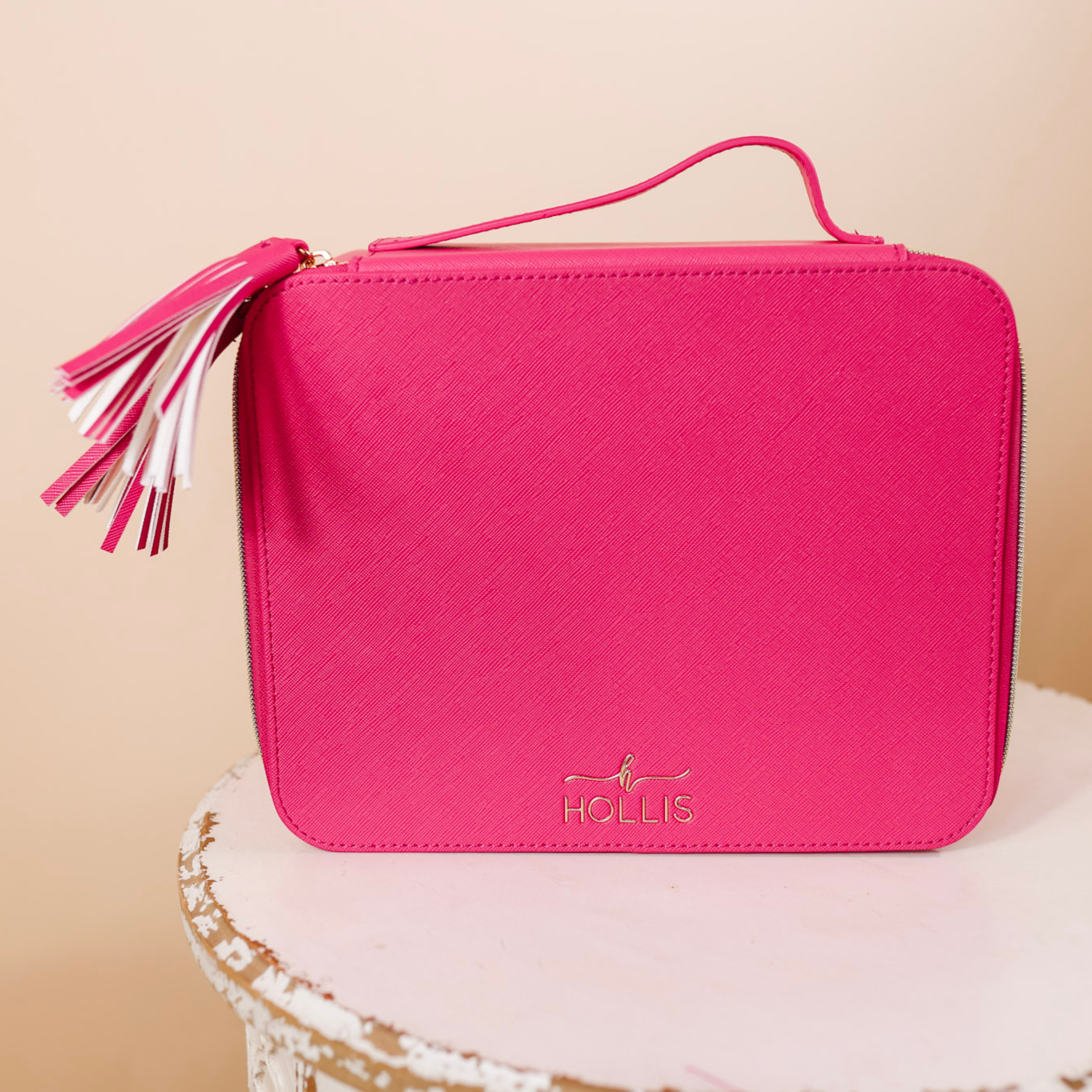 A hot pink bag with a tassel  is sitting in the center of the picture. Background is solid tan. 
