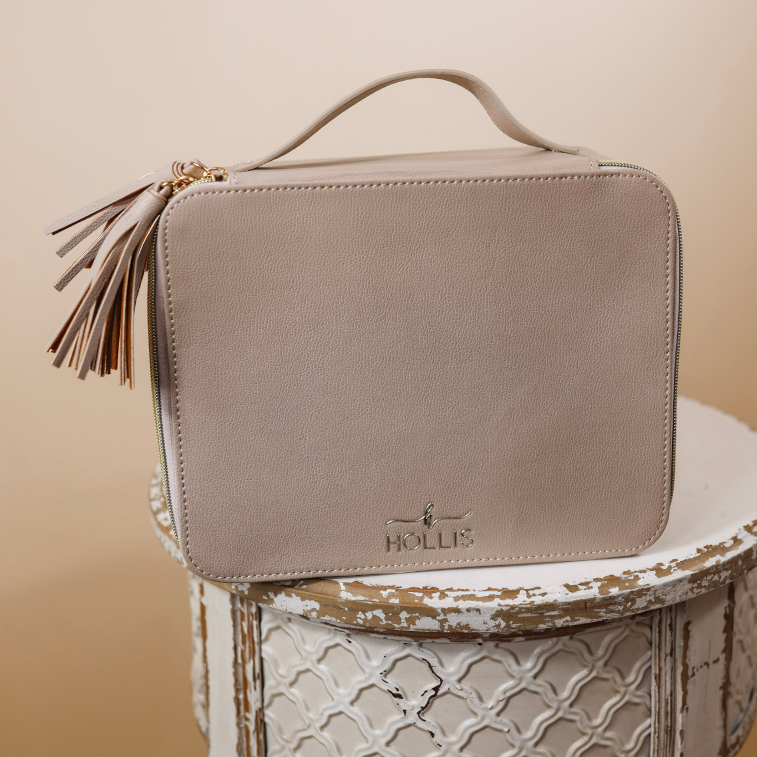 A nude bag with a handle and tassel is sitting in the middle of the picture. Background is solid tan.