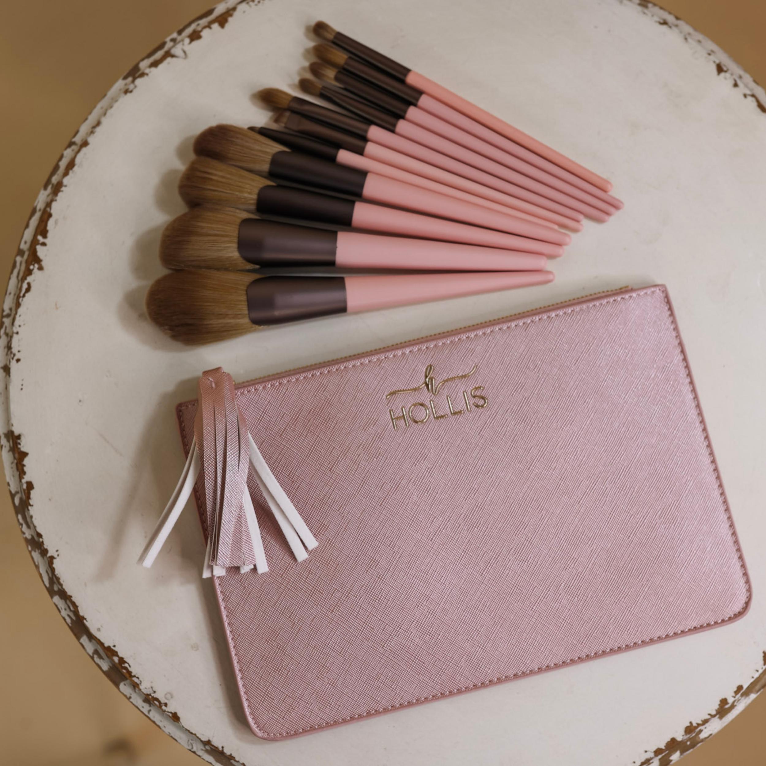 A blush pouch is laid in the bottom of the picture with 11 different sized makeup brushes across the top of the pouch in pink and brown. Background is white.  
