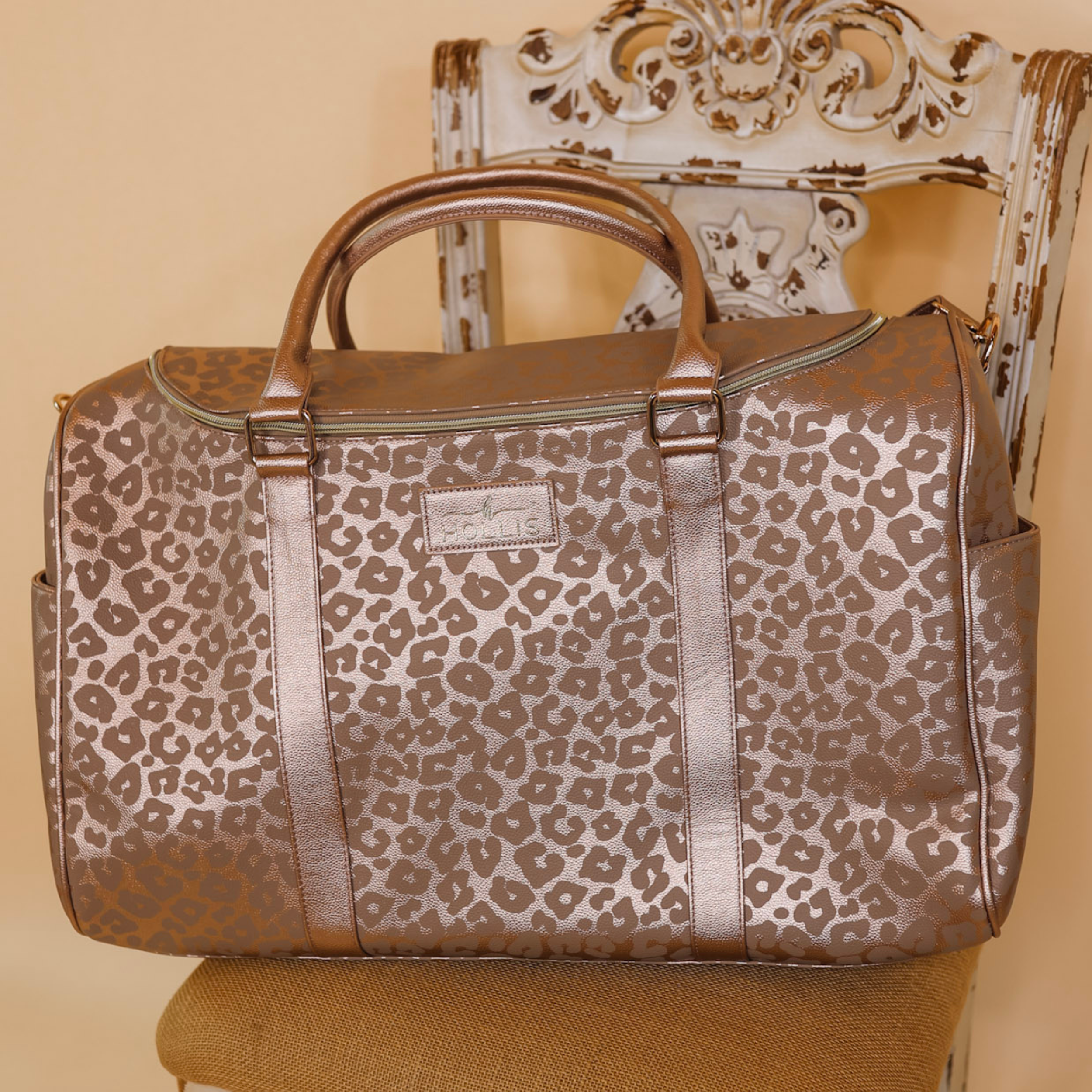 A large weekender bag is set on a chair in a leopard print. The background is solid tan. 
