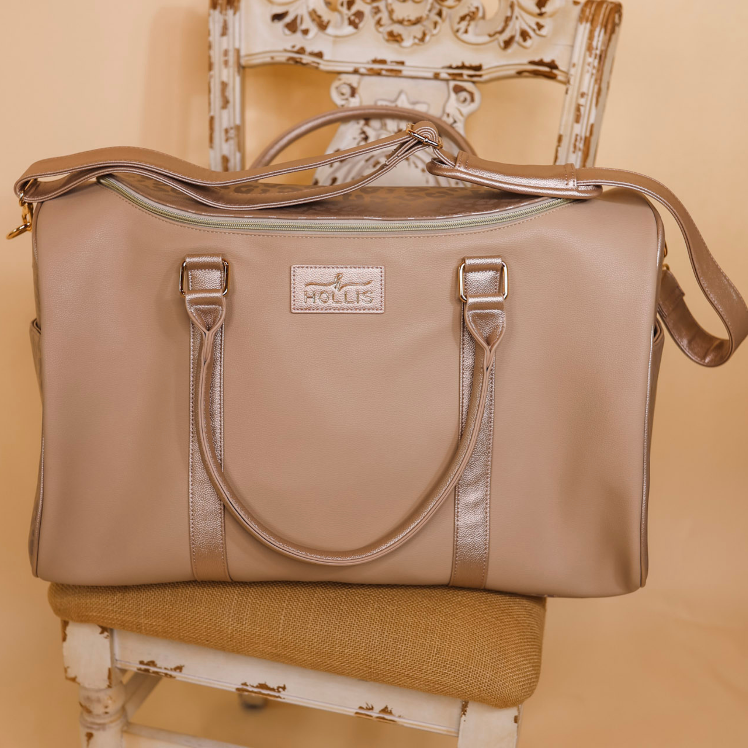 A large nude weekender bag is set on a chair in the middle of the picture. Background is solid tan. 