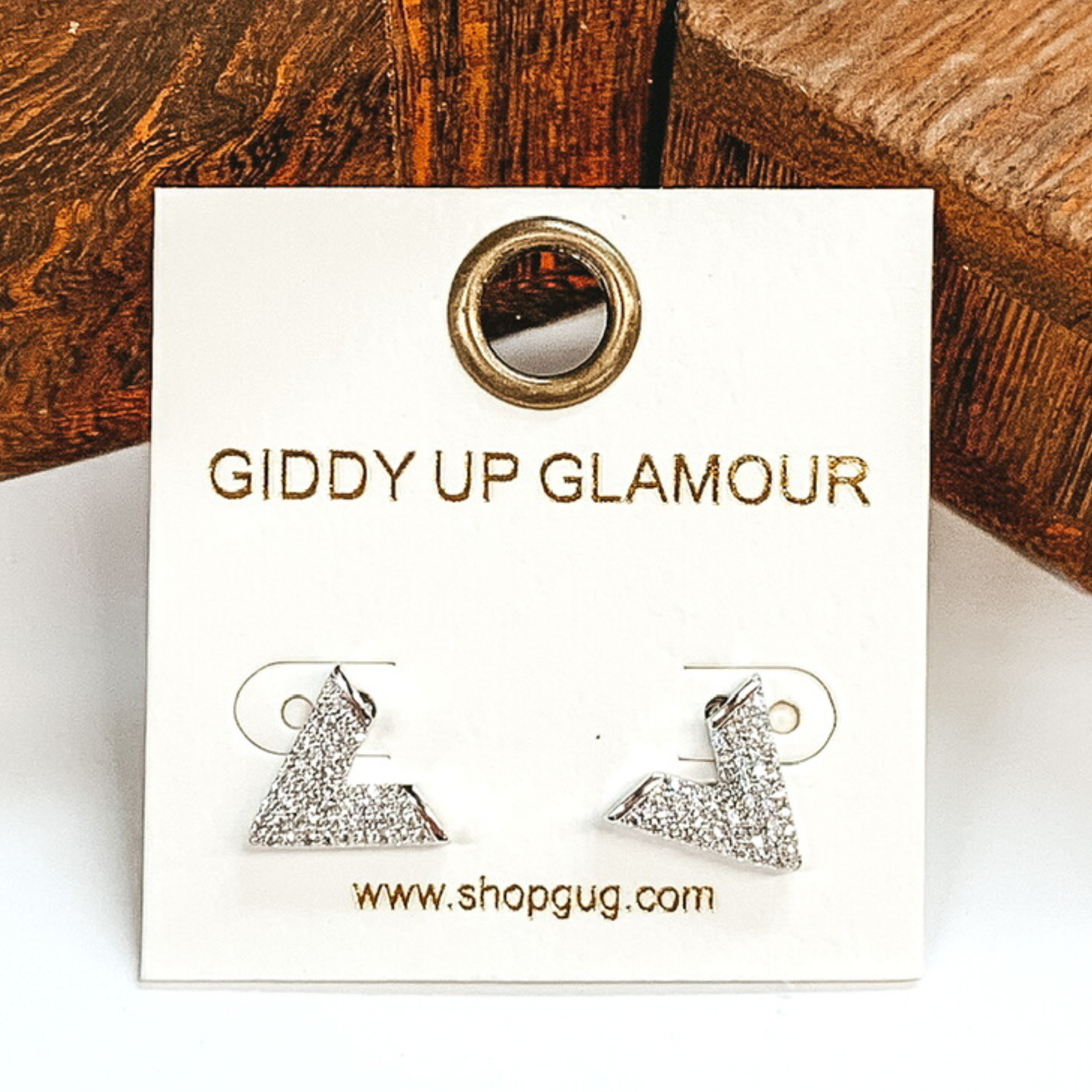 Small, silver "V" shaped stud earrings with clear crystals. These earrings are pictured on a white earrings card on a white and brown background.