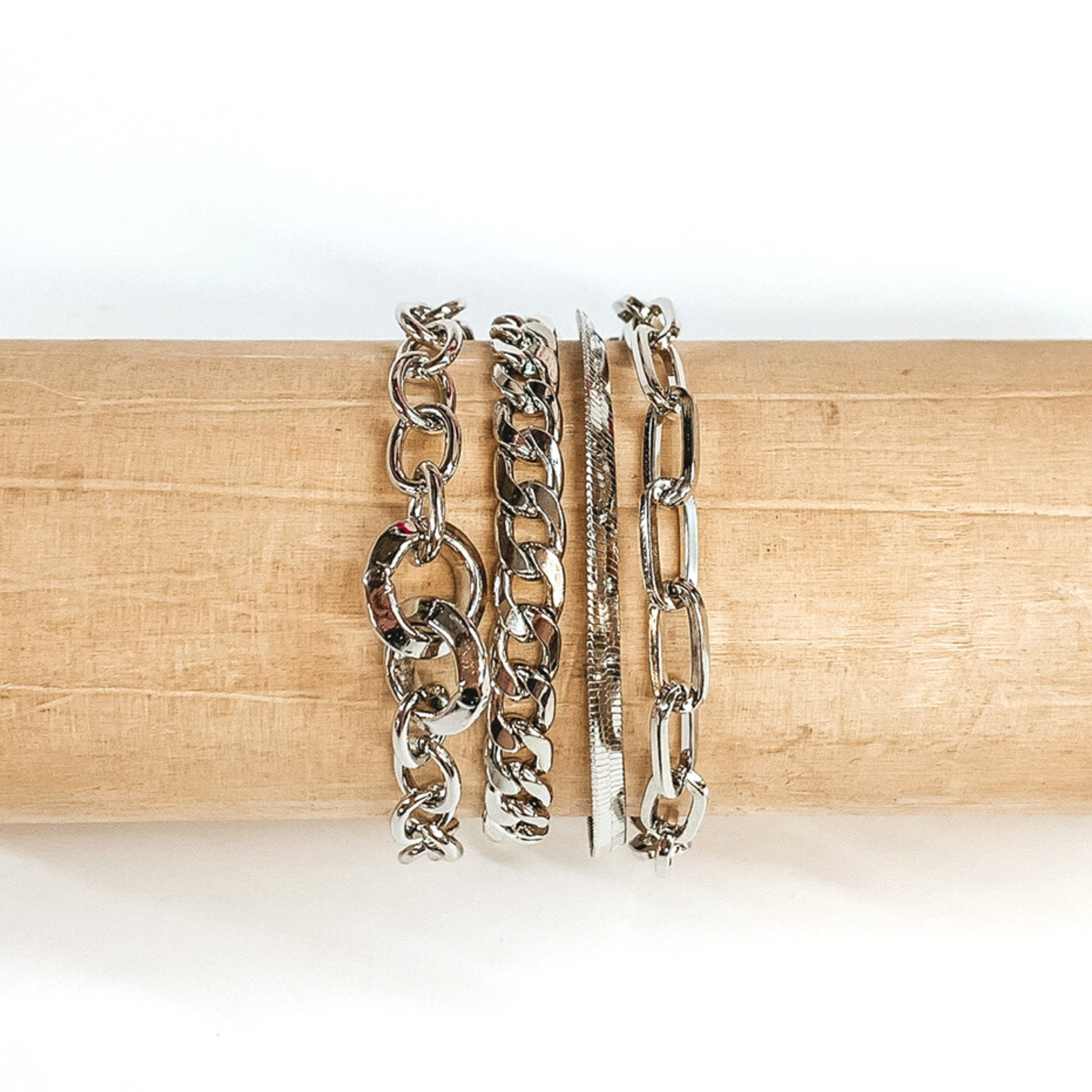 Four stranded silver bracelet pictured on a wood bracelet holder on a white background. This bracelet includes a paperclip chain, a curb chain, and a snacke chain, and a circle chain with two bigger chain  links. 